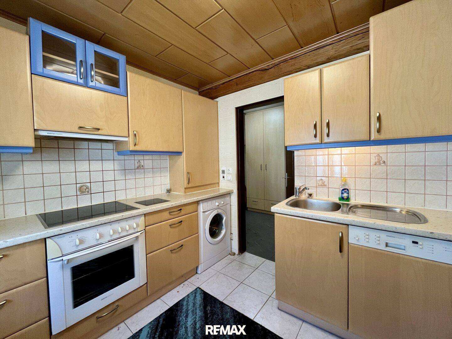 Funktionale Küche mit Holzschränken, Fliesenboden und integrierter Waschmaschine.