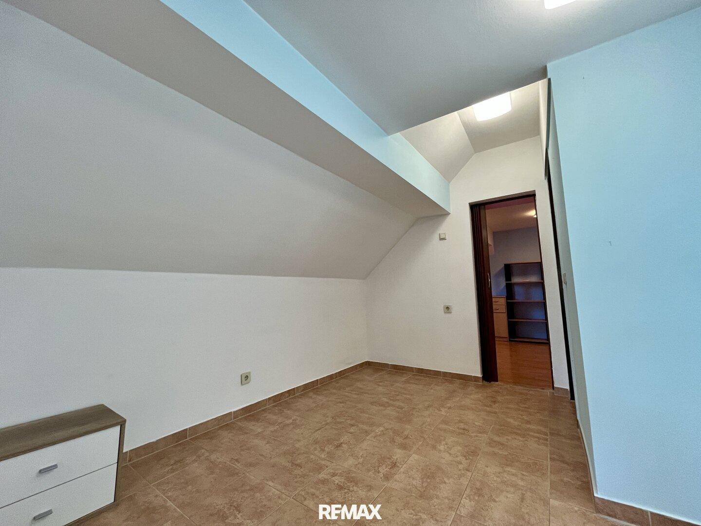 Helles Zimmer im Dachgeschoss mit Fliesenboden und Dachschrägen.