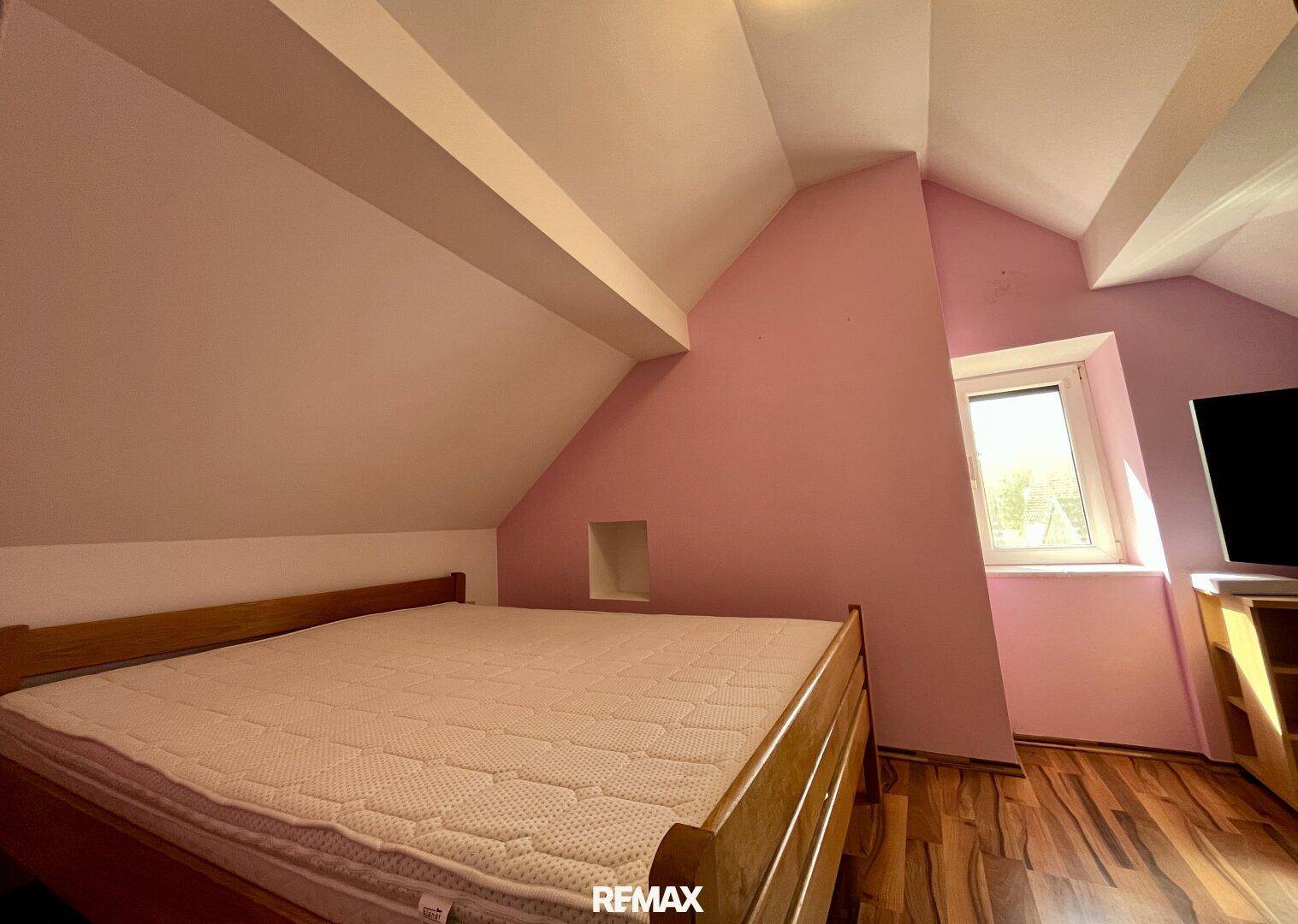 Gemütliches Schlafzimmer im Dachgeschoss mit Dachschrägen und Holzbett.