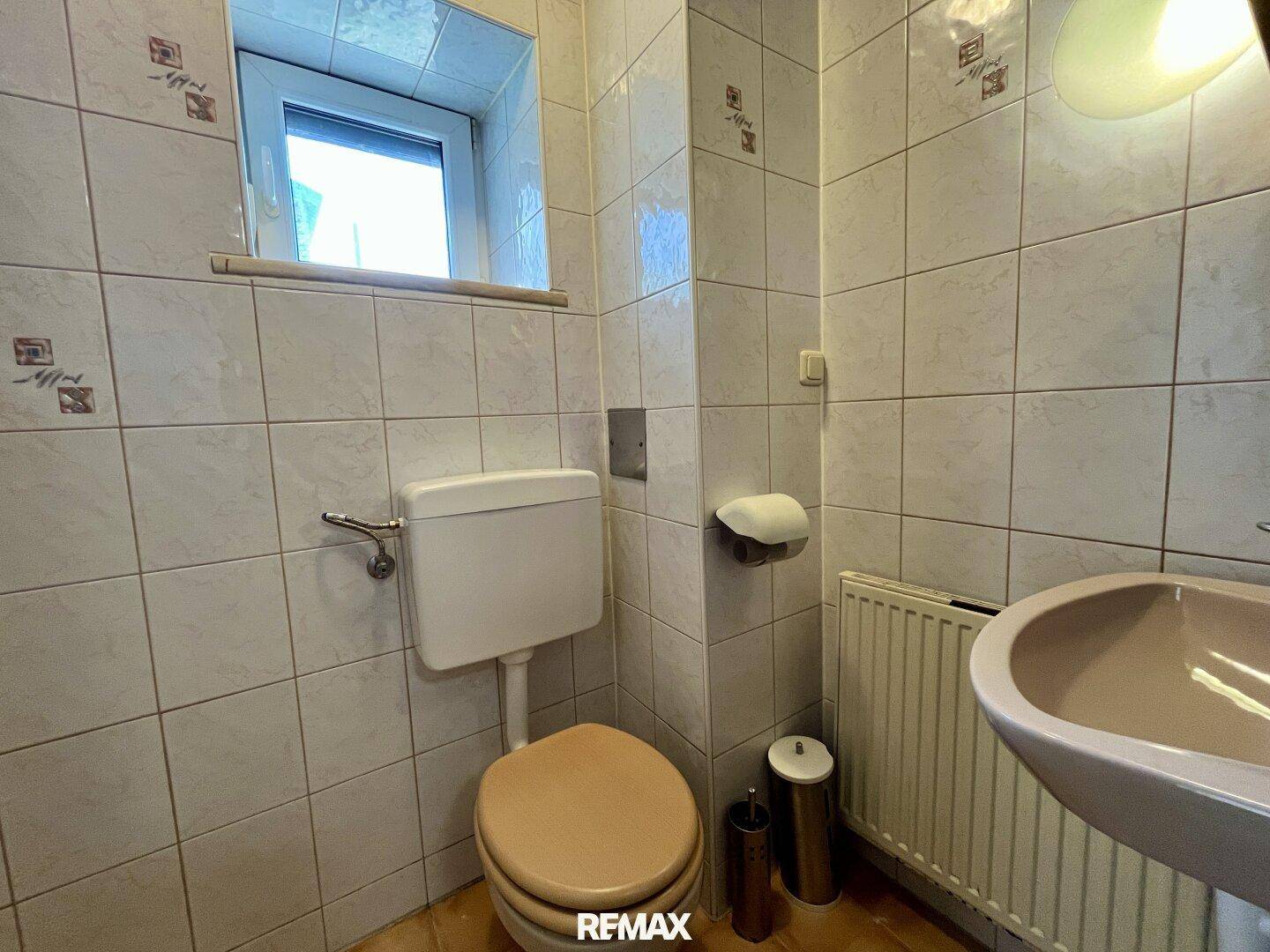 Kleines WC mit Fliesen an Wänden und Boden, ausgestattet mit Fenster und Heizung.