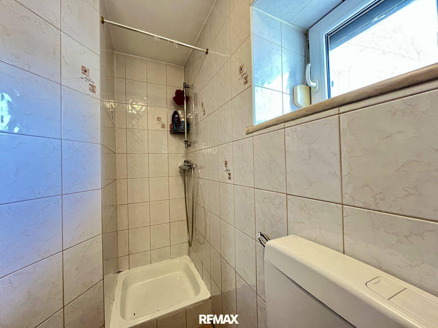 Kleines Badezimmer mit Duschkabine, WC und Fenster, komplett gefliest.