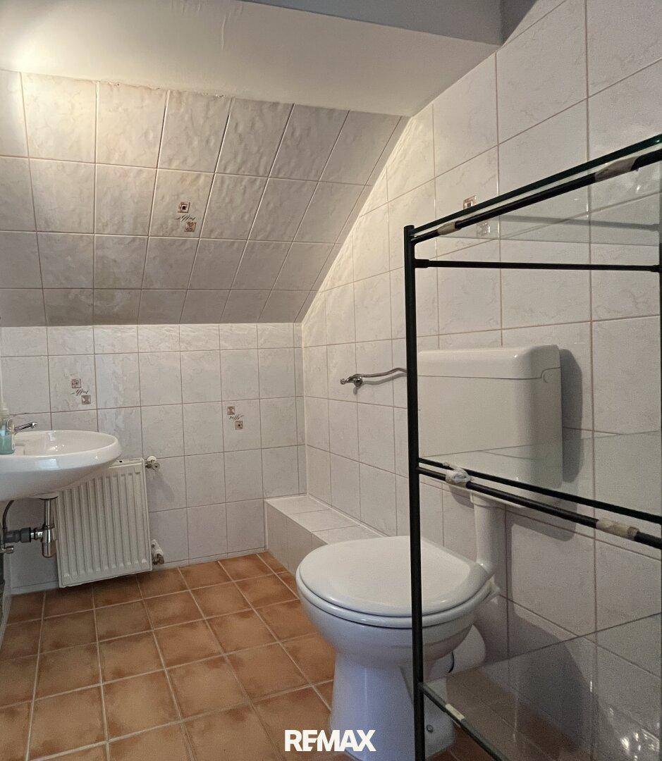Badezimmer im Dachgeschoss mit Dachschräge, WC, Waschbecken und Fliesenboden.