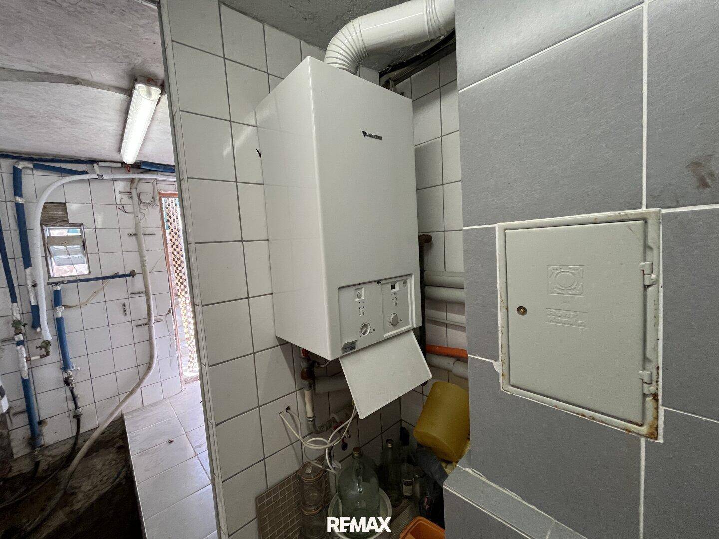 Heizungsraum mit Gastherme, Fliesenwänden und sichtbaren Rohrleitungen.