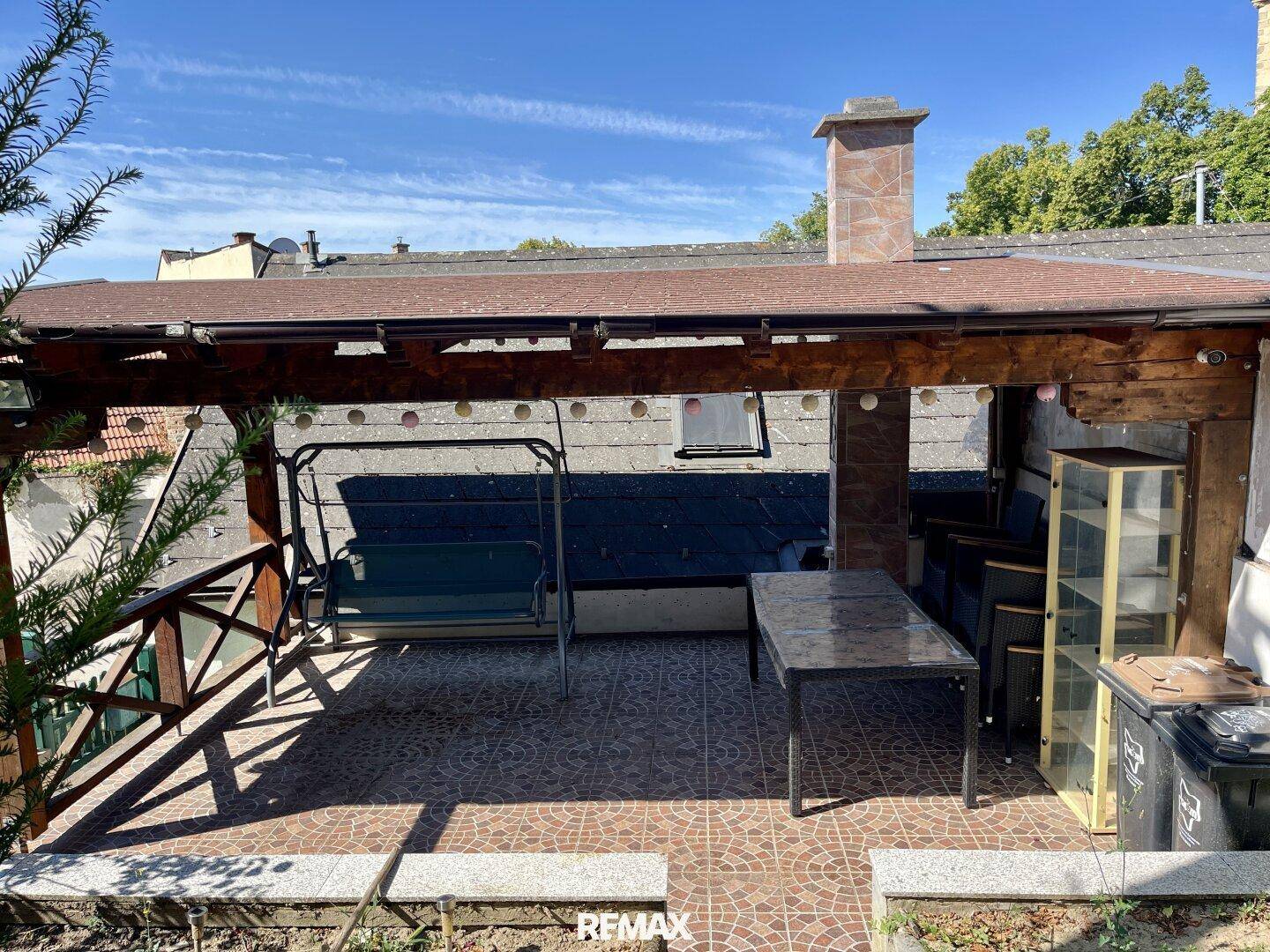 Überdachte Terrasse mit Fliesenboden, Schaukel und Tisch für den Außenbereich.
