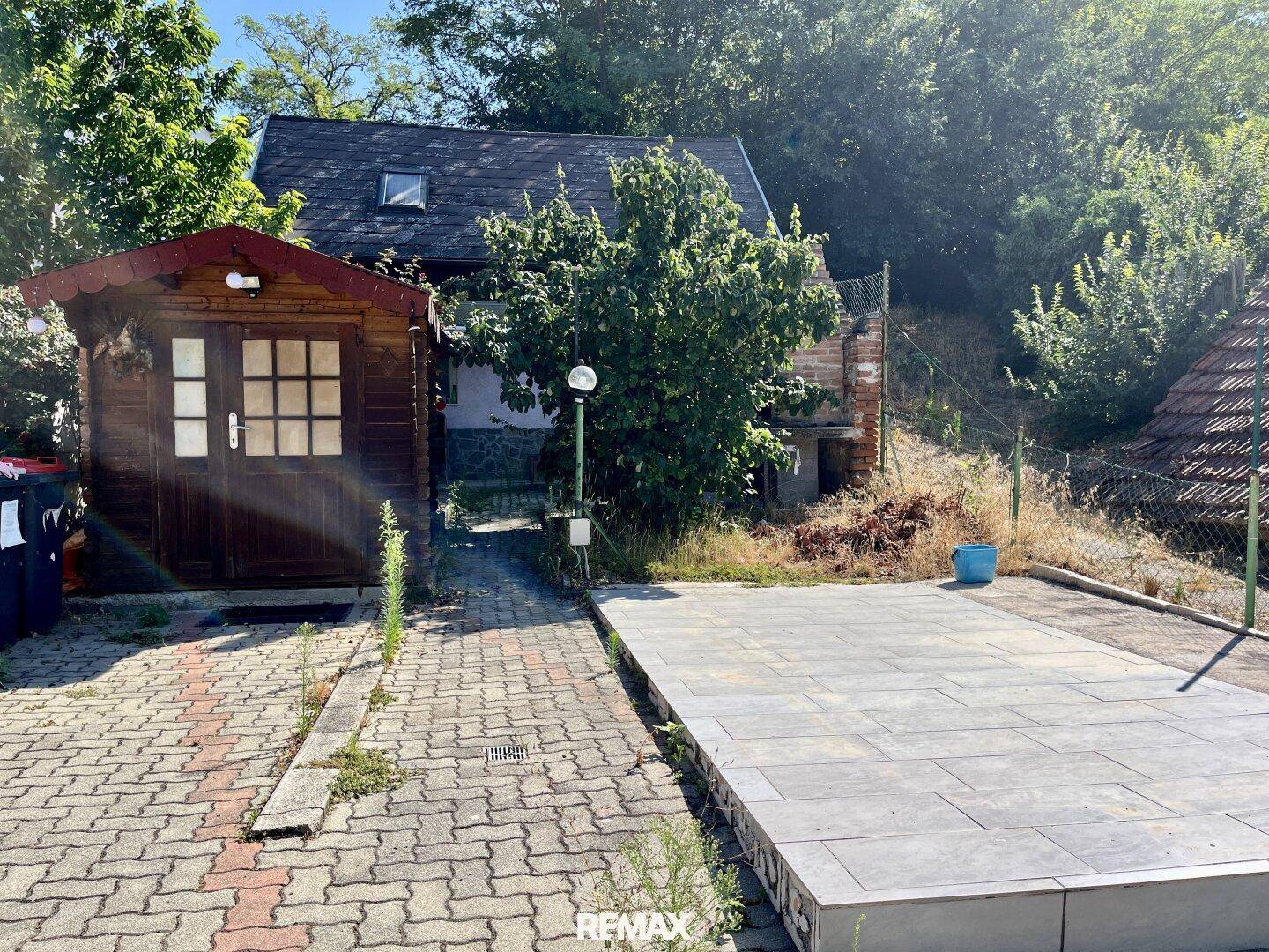 Gartenbereich mit einem Holzschuppen und gepflasterter Fläche vor dem Haus.