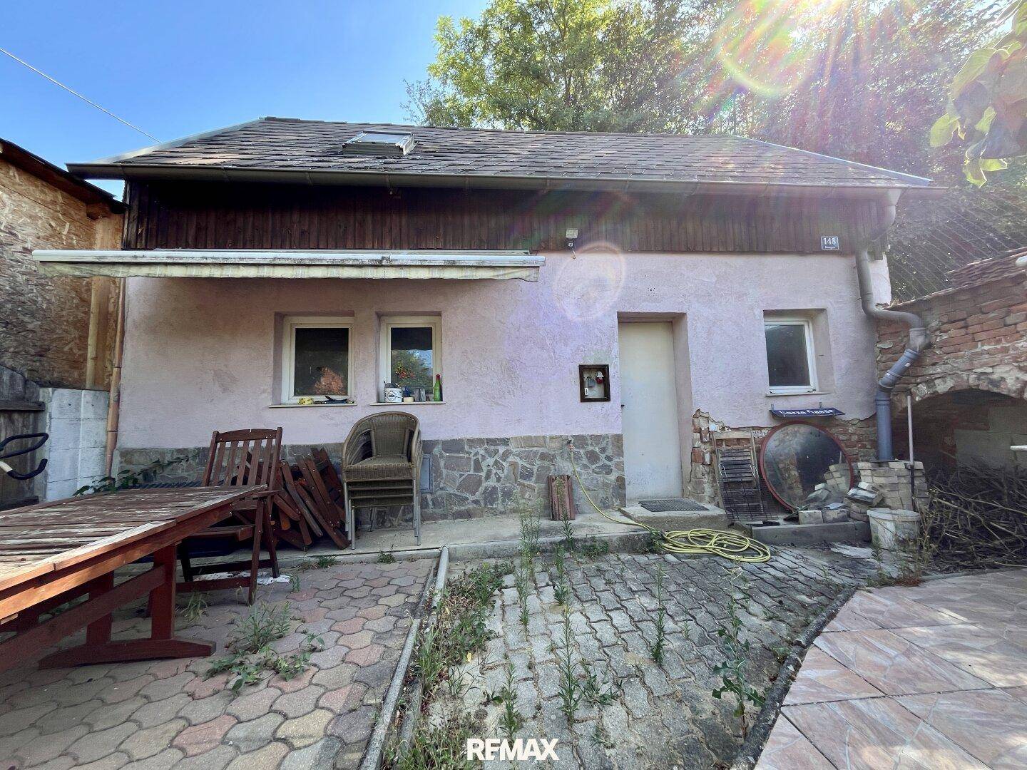Rückseite des Hauses mit gepflastertem Außenbereich und rustikalen Möbeln.