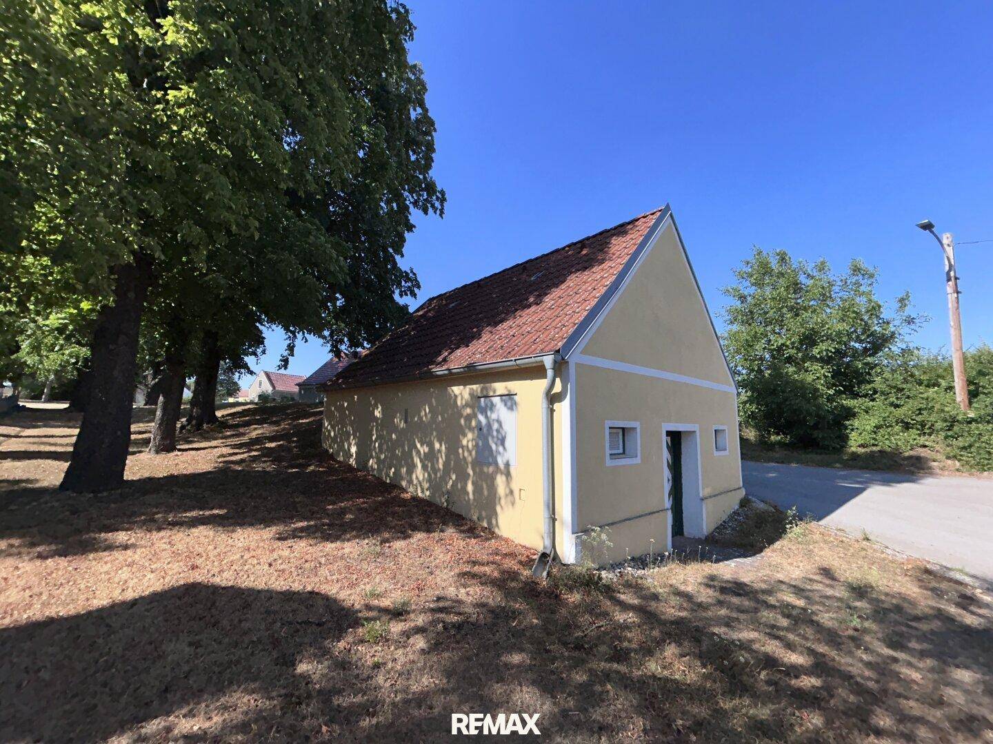 Seitenansicht des gelben Gebäudes mit Bäumen und trockenem Gras in ländlicher Umgebung.