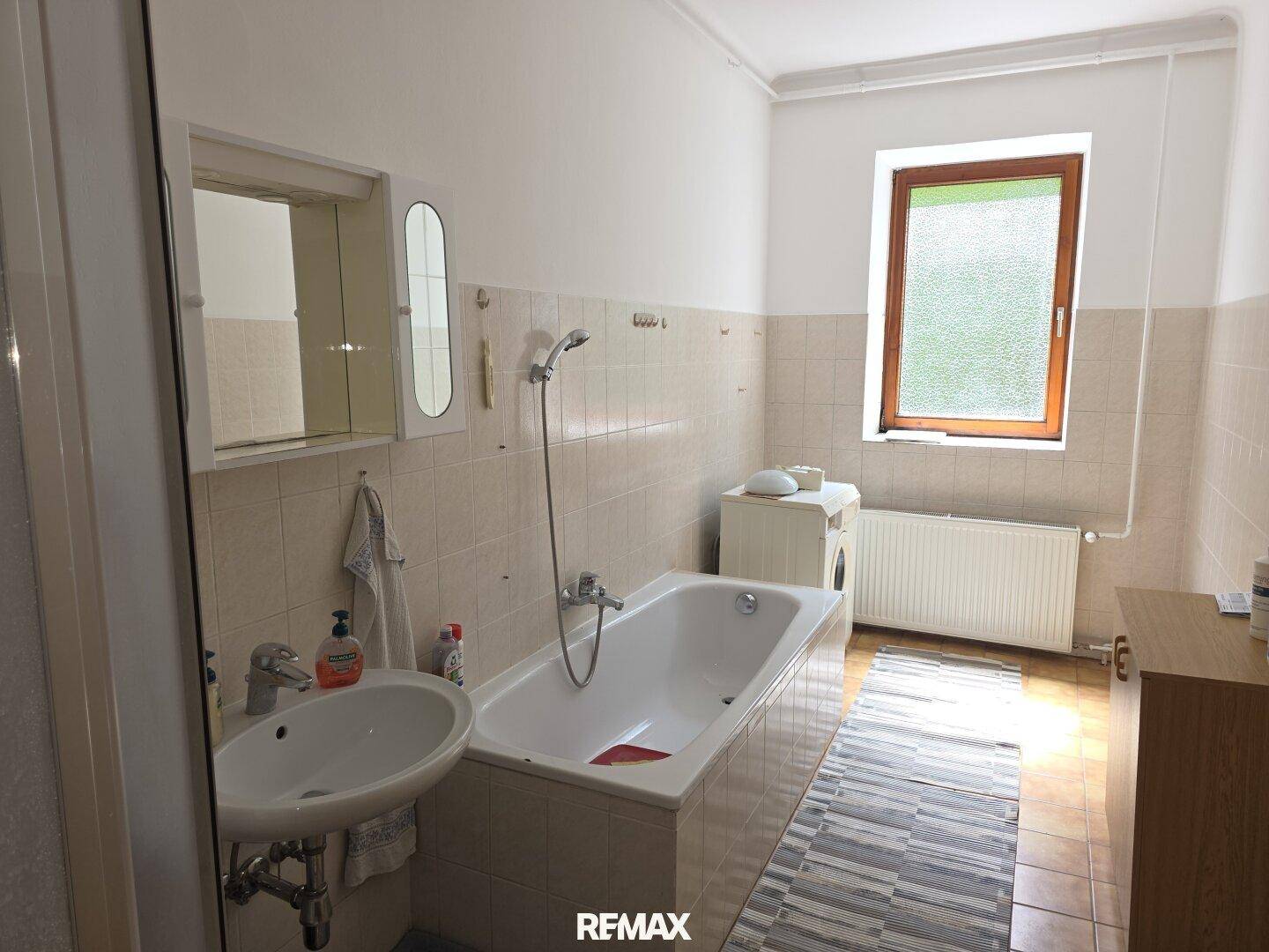 Badezimmer mit Badewanne, Waschbecken und Fenster, in hellem Fliesendesign.