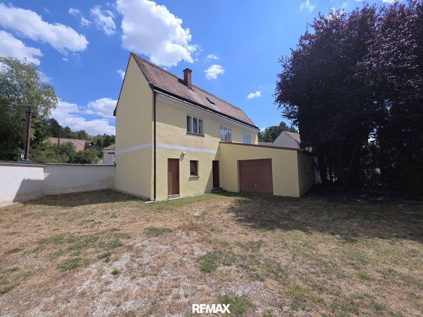 Rückseite des Hauses mit integrierter Garage und großem, sonnigen Gartenbereich.