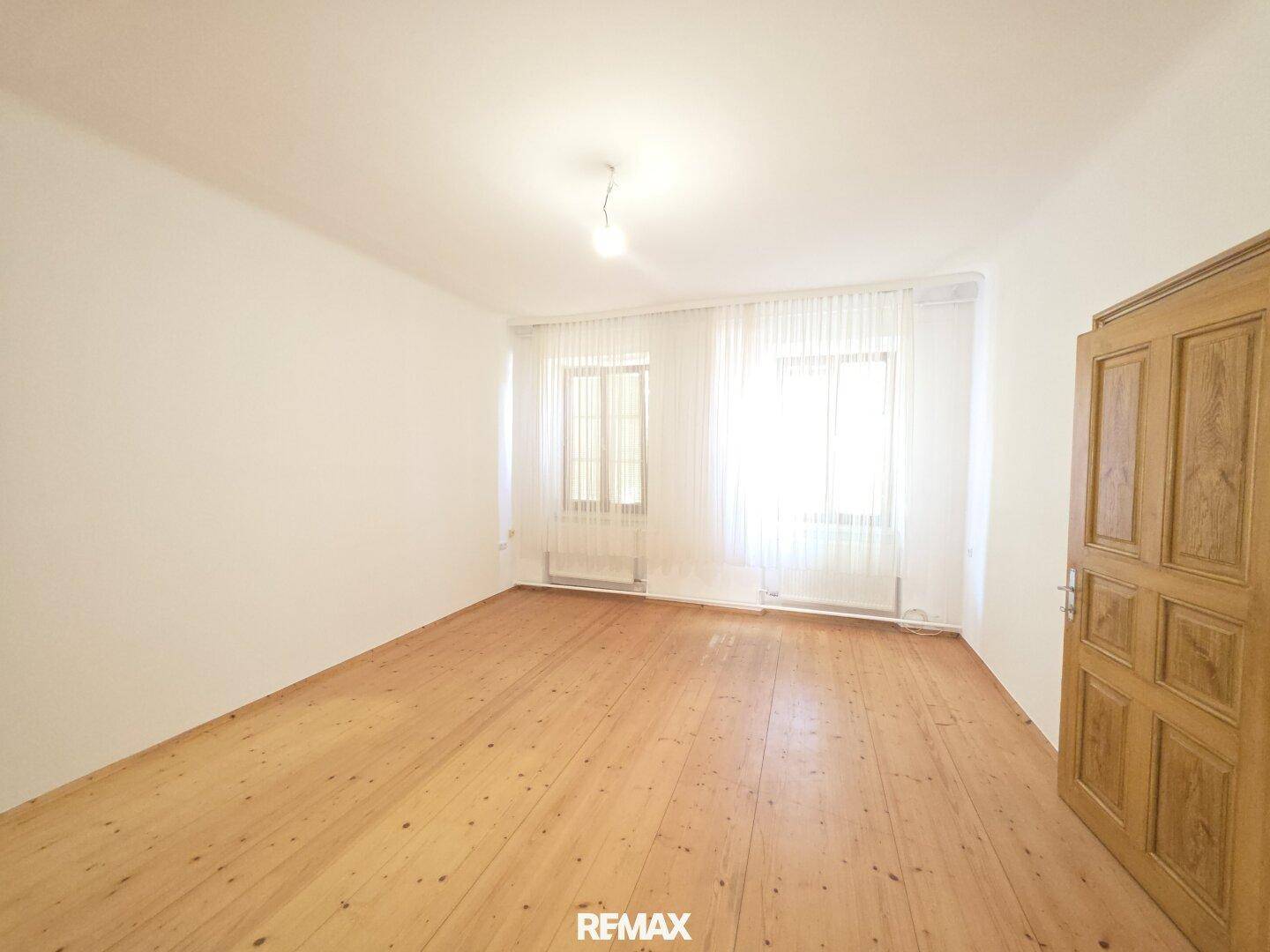 Helles Schlafzimmer mit Holzdielenboden und zwei großen Fenstern, unmöbliert.