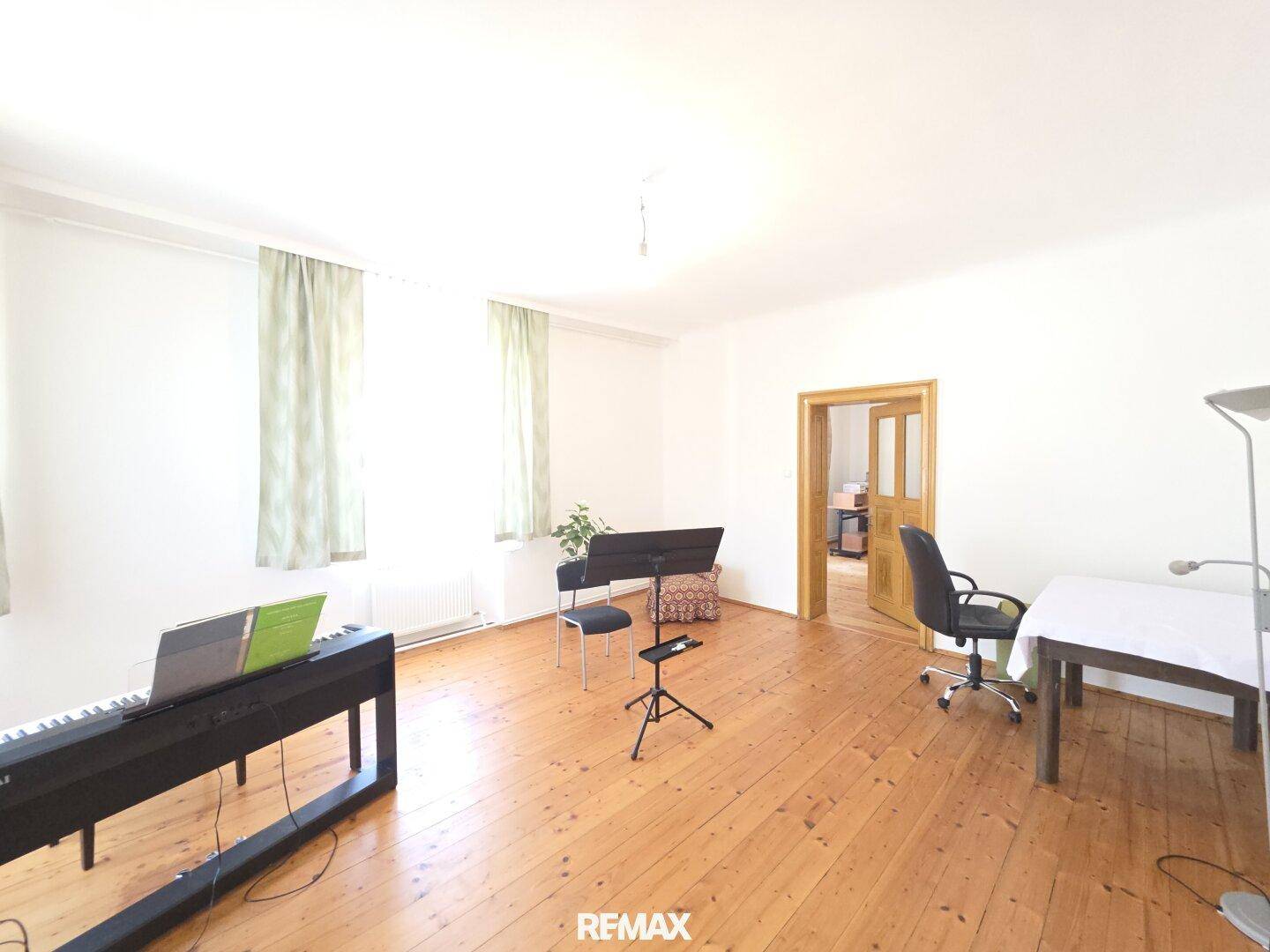 Geräumiges Zimmer mit Holzdielenboden, Klavier und Schreibtisch, ideal als Arbeitszimmer.