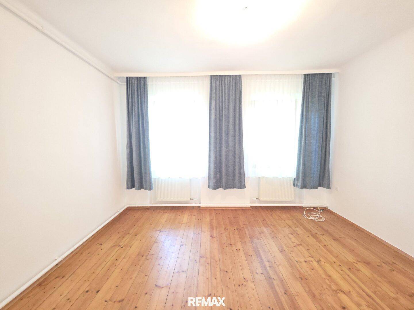Leeres Zimmer mit Holzdielenboden und großen Fenstern, bereit zur individuellen Gestaltung.