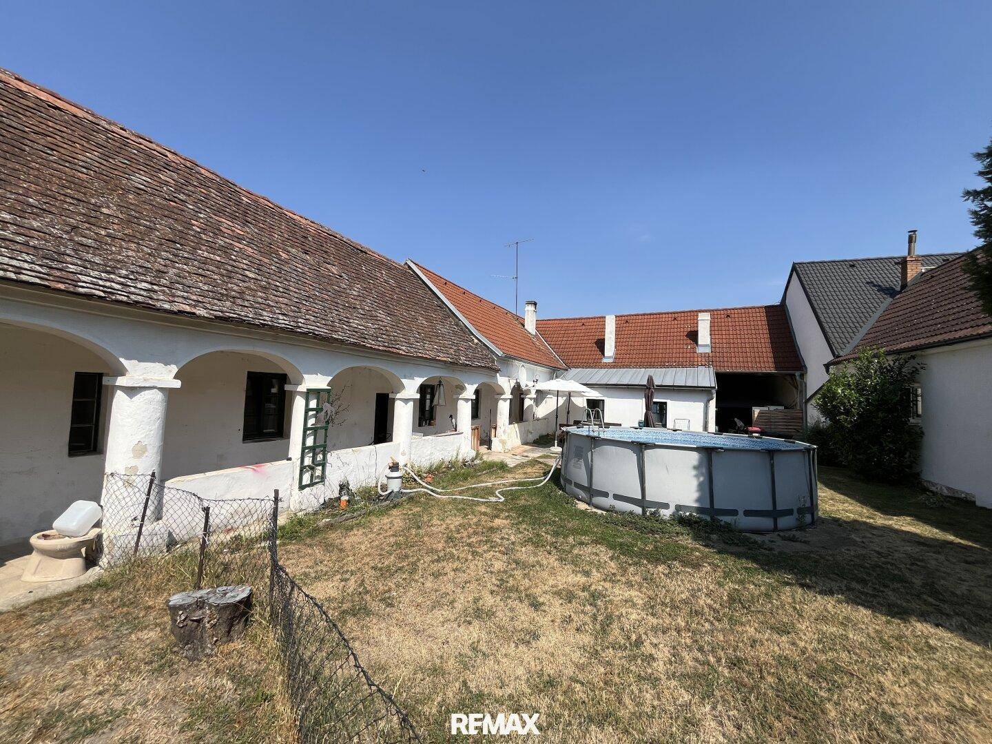 Großer Garten mit aufgestelltem Pool und der Rückseite des Hauses mit Arkaden.