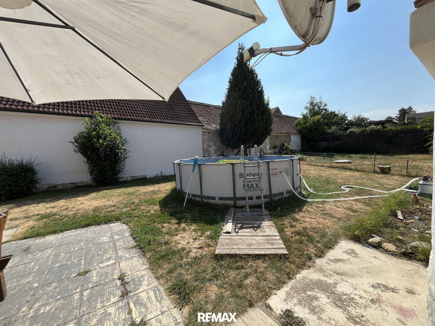 Sonniger Gartenbereich mit einem aufgestellten Pool und einer kleinen Holztreppe.