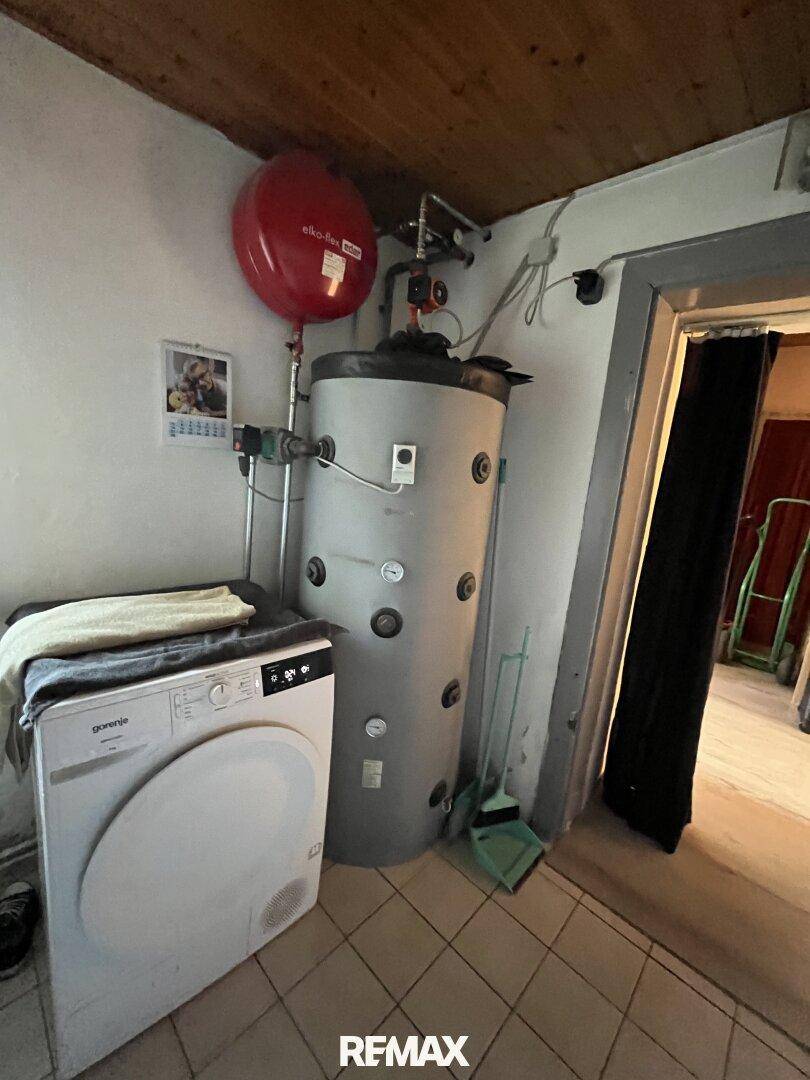 Hauswirtschaftsraum mit Waschmaschine, Warmwasserspeicher und Fliesenboden.