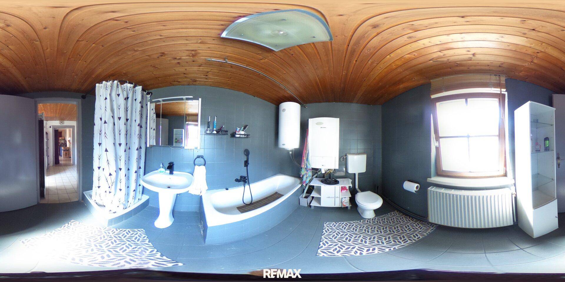 Badezimmer mit Badewanne, Waschbecken, WC und Duschvorhang, unter einer Holzdeckenverkleidung.