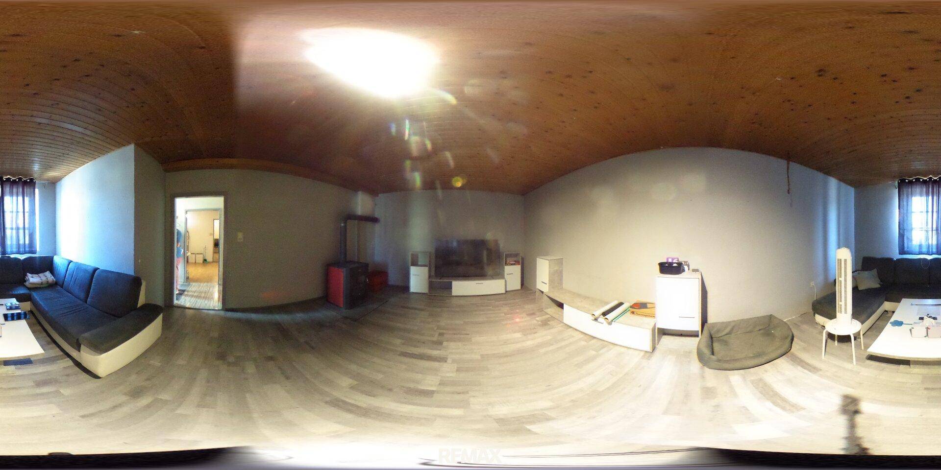 Geräumiges Wohnzimmer mit bequemer Couch, Fernseher und charakteristischer Holzdeckenverkleidung.