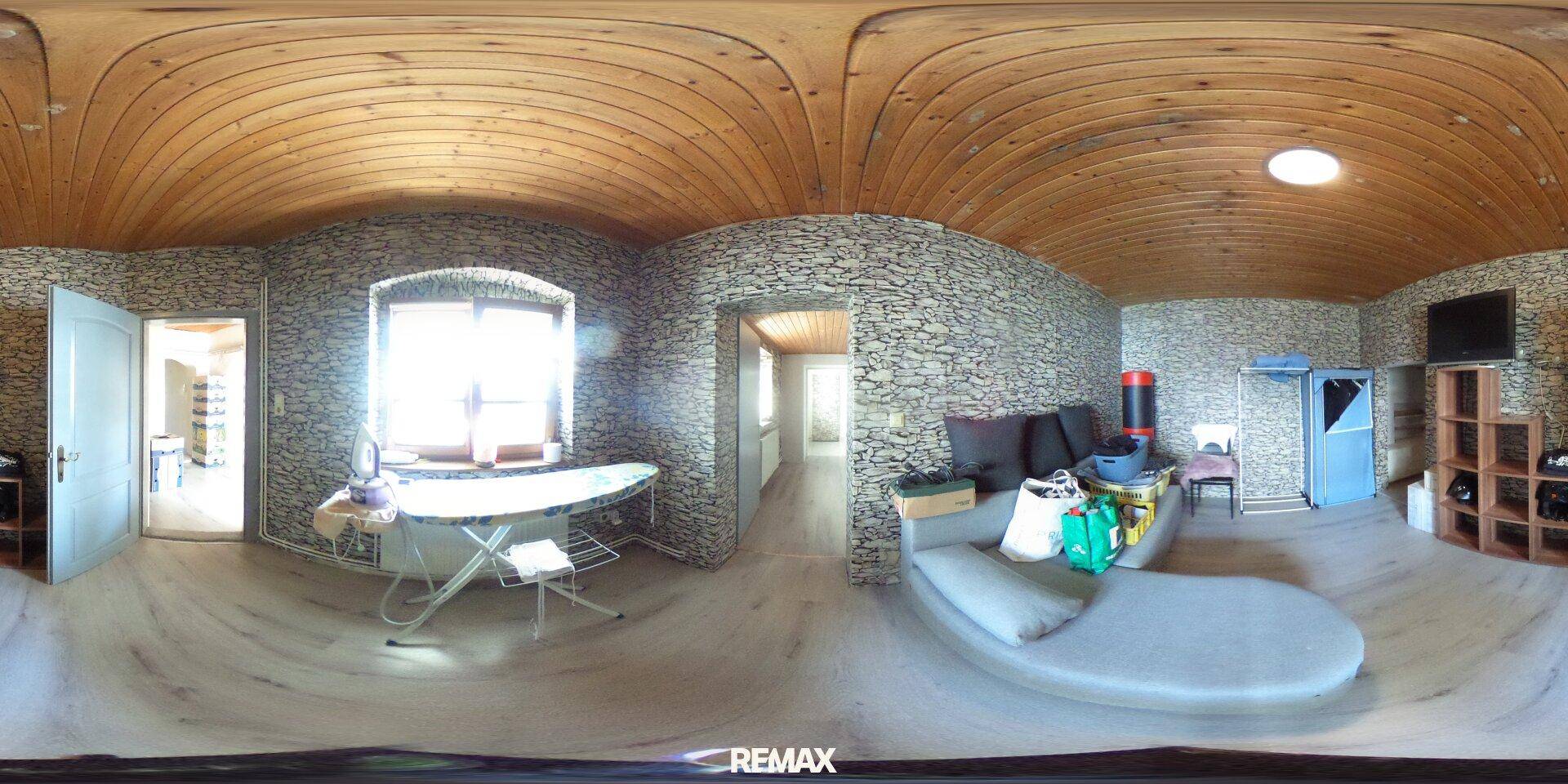 Gemütlicher Wohnbereich mit geschwungener Couch, Fenster und dekorativer Steinwand unter Holzdecke.