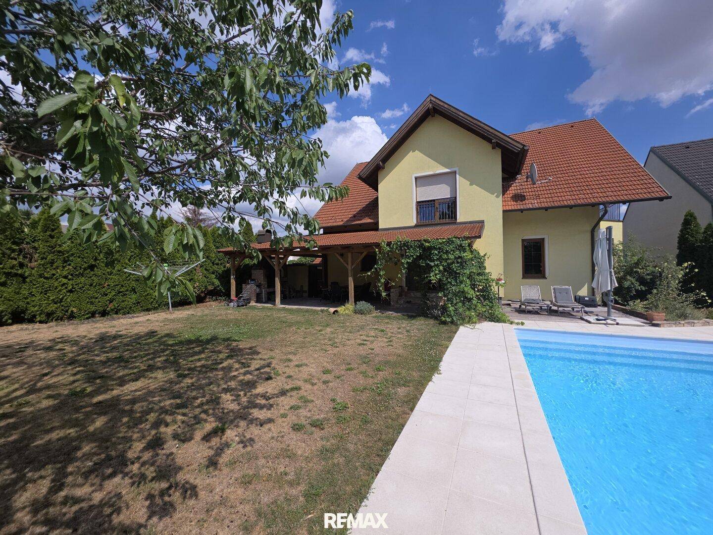Weitläufiger Garten mit erfrischendem Pool und schattenspendenden Bäumen an einem sonnigen Tag.