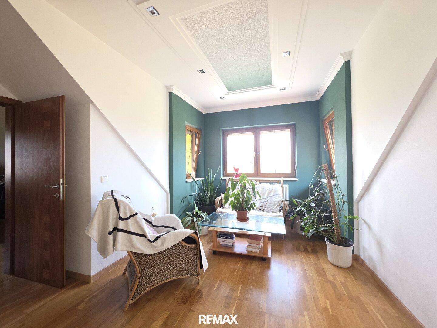 Gemütlicher Sitzbereich mit Korbsessel, vielen Pflanzen und natürlichem Lichteinfall durch die Fenster.