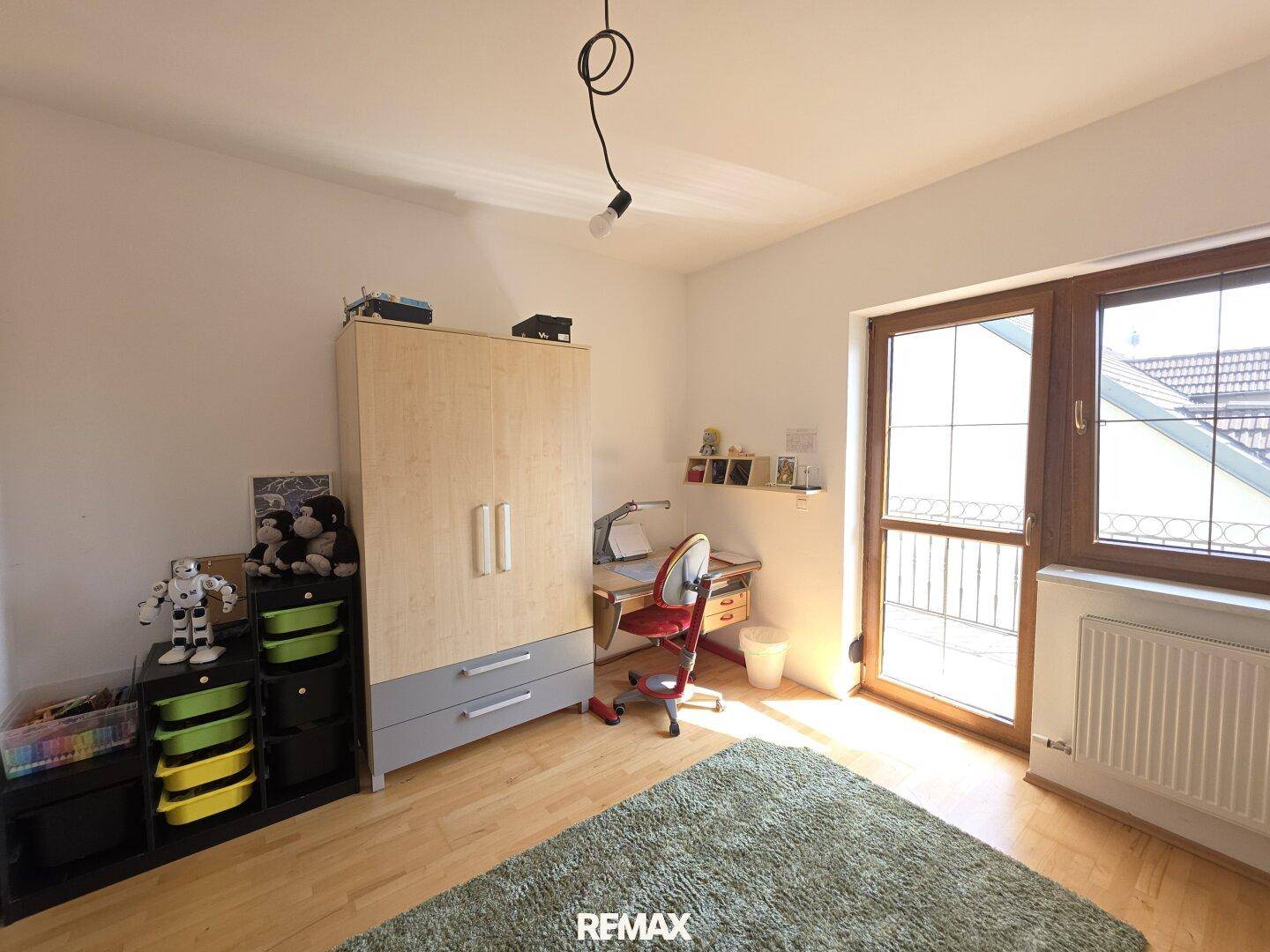 Kinderzimmer mit Holzboden, großem Fenster und einem Kleiderschrank.