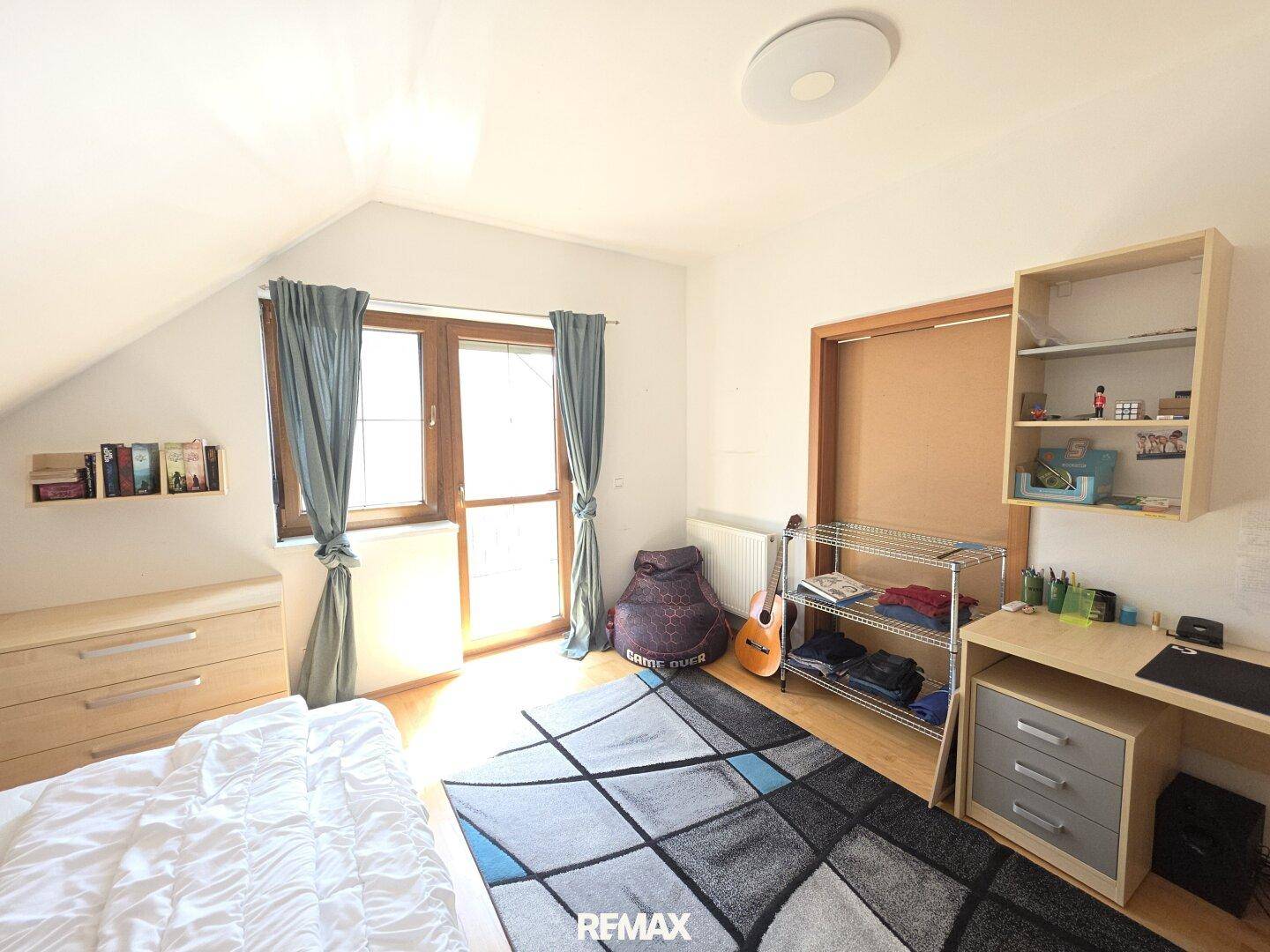 Helles Schlafzimmer mit Holzboden, großem Fenster und einem Schreibtischbereich.