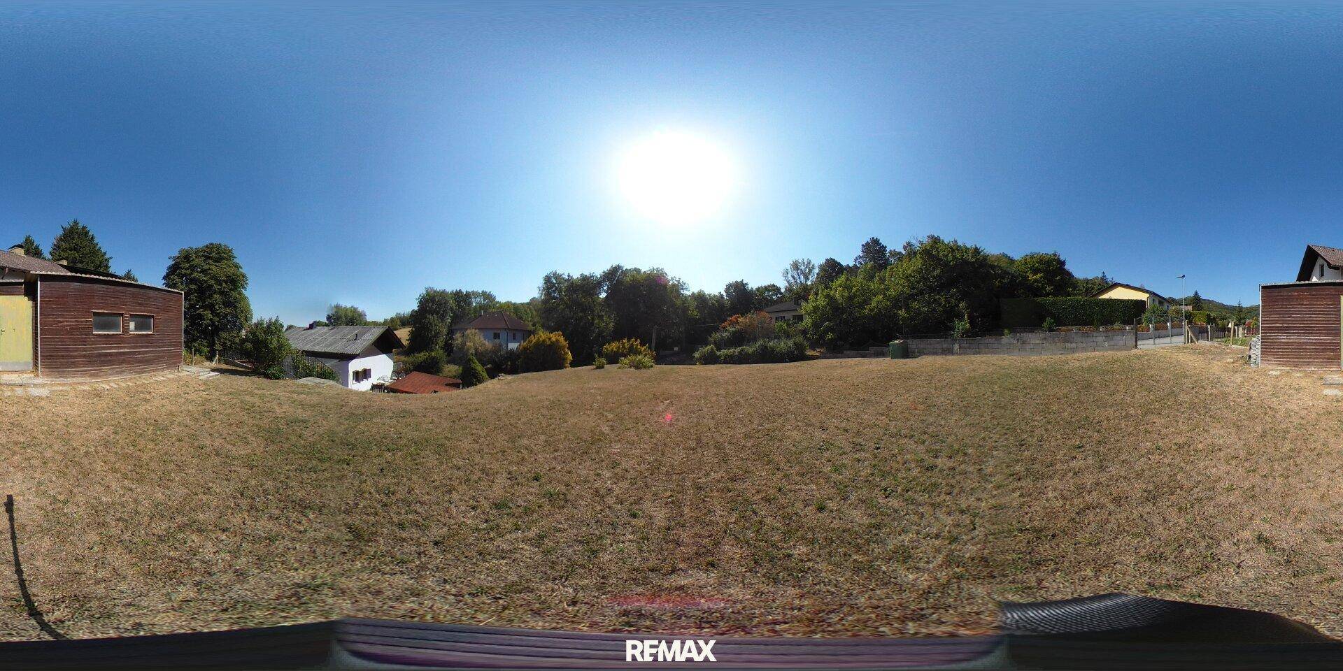 Weitläufiges, sonniges Grundstück mit trockenem Gras und Bäumen im Hintergrund.