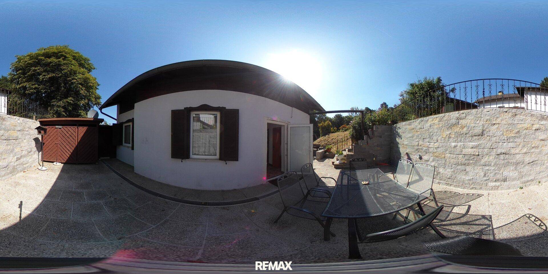 Sonnige Terrasse vor einem kleinen Haus mit Gartenmöbeln und einer Feuerstelle.