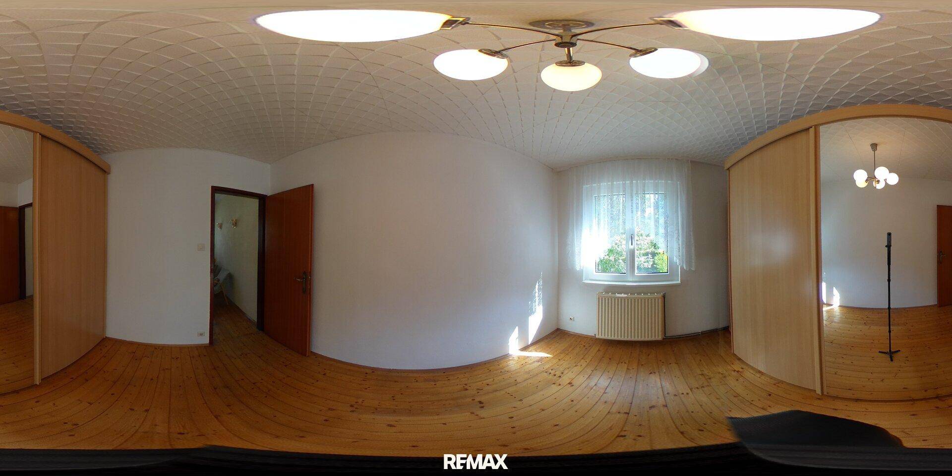 Helles Schlafzimmer mit Parkettboden, weiß gestrichenen Wänden und großem Fenster.