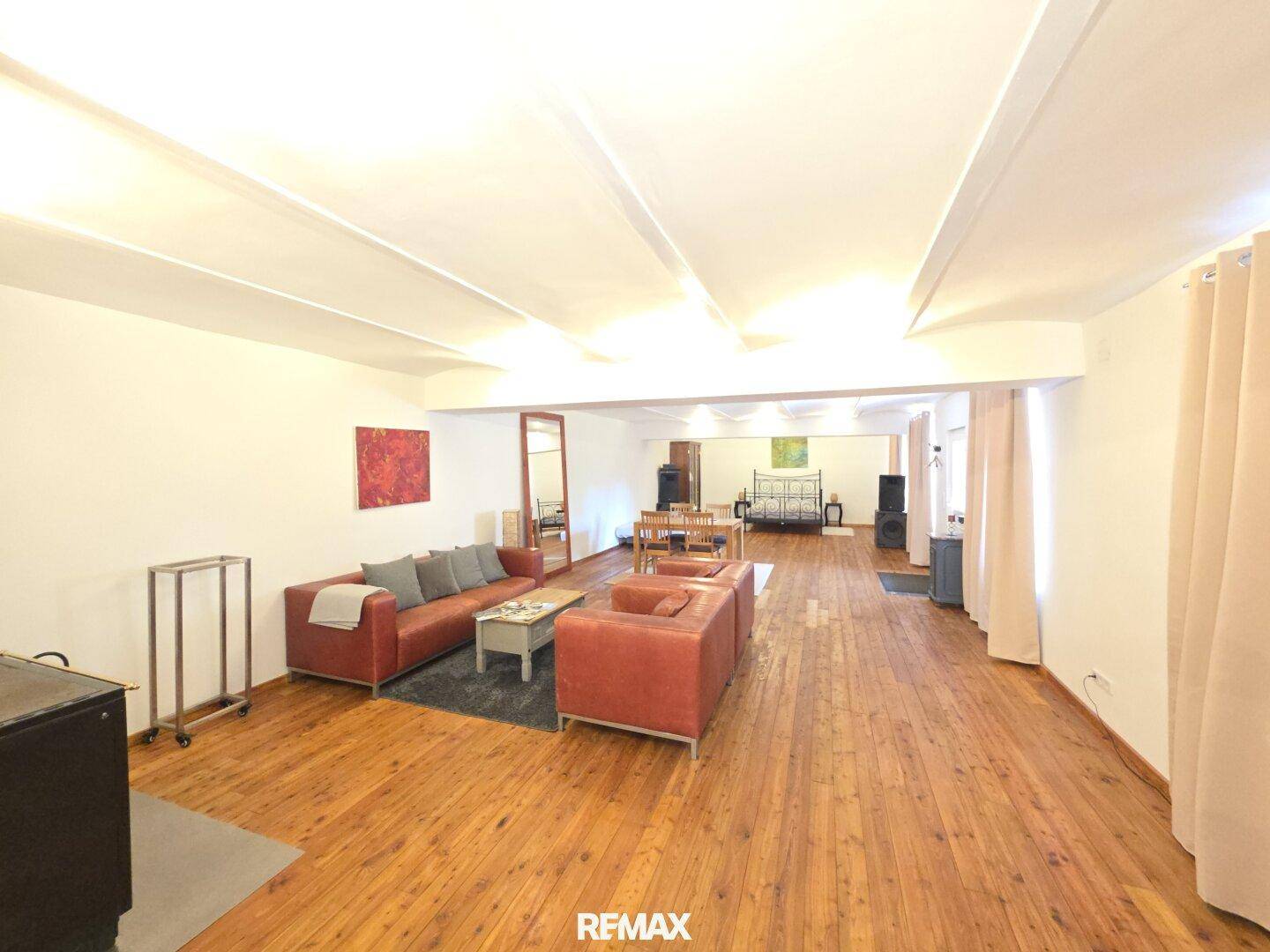 Großer offener Wohnbereich mit Holzboden, Ledersofas und sichtbaren Deckenbalken.
