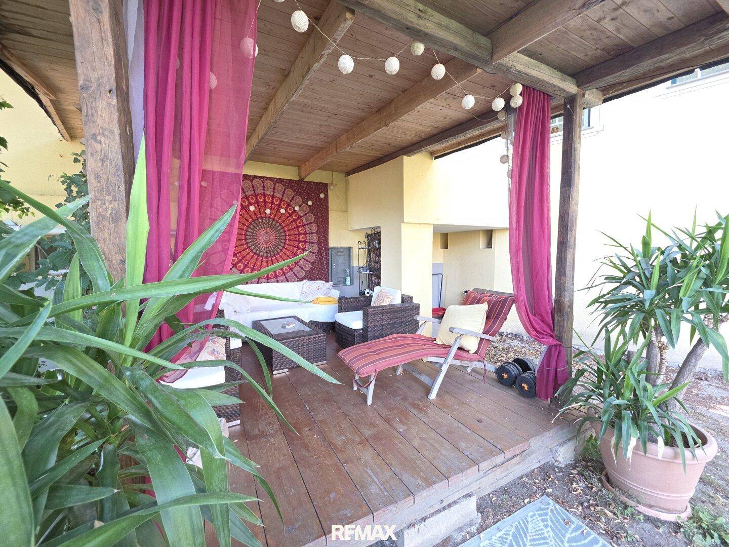 Gemütliche überdachte Terrasse mit Holzdeck, Loungemöbeln und farbigen Vorhängen für entspannte Stunden.