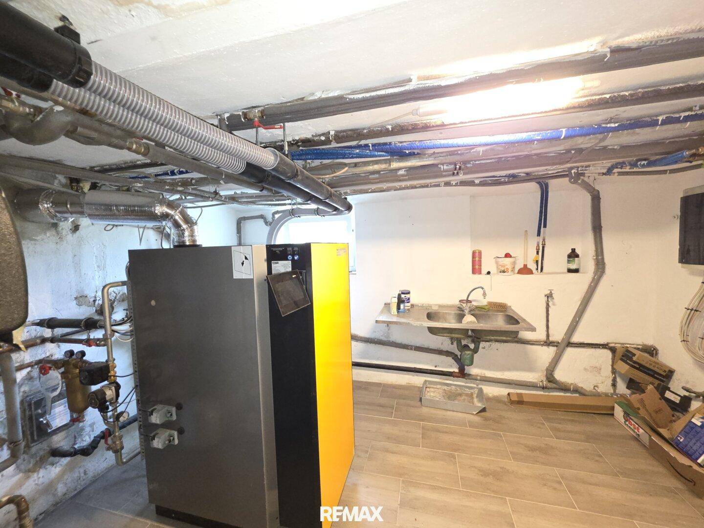 Heizungsraum im Keller mit moderner Heizungsanlage, sichtbaren Rohren und einem Waschbecken.