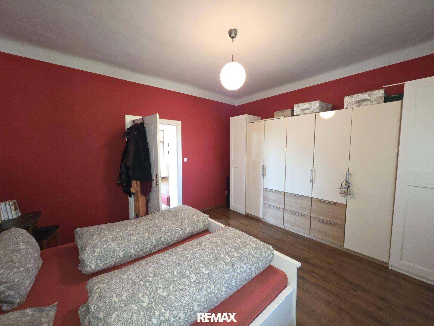 Schlafzimmer mit roter Akzentwand, Doppelbett und großem Kleiderschrank.