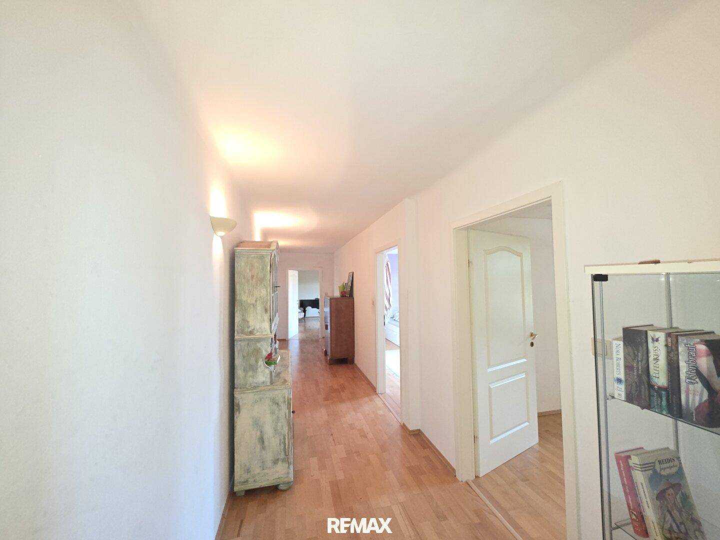 Heller Flur mit Holzboden, weiß gestrichenen Wänden und einem antiken Schrank.