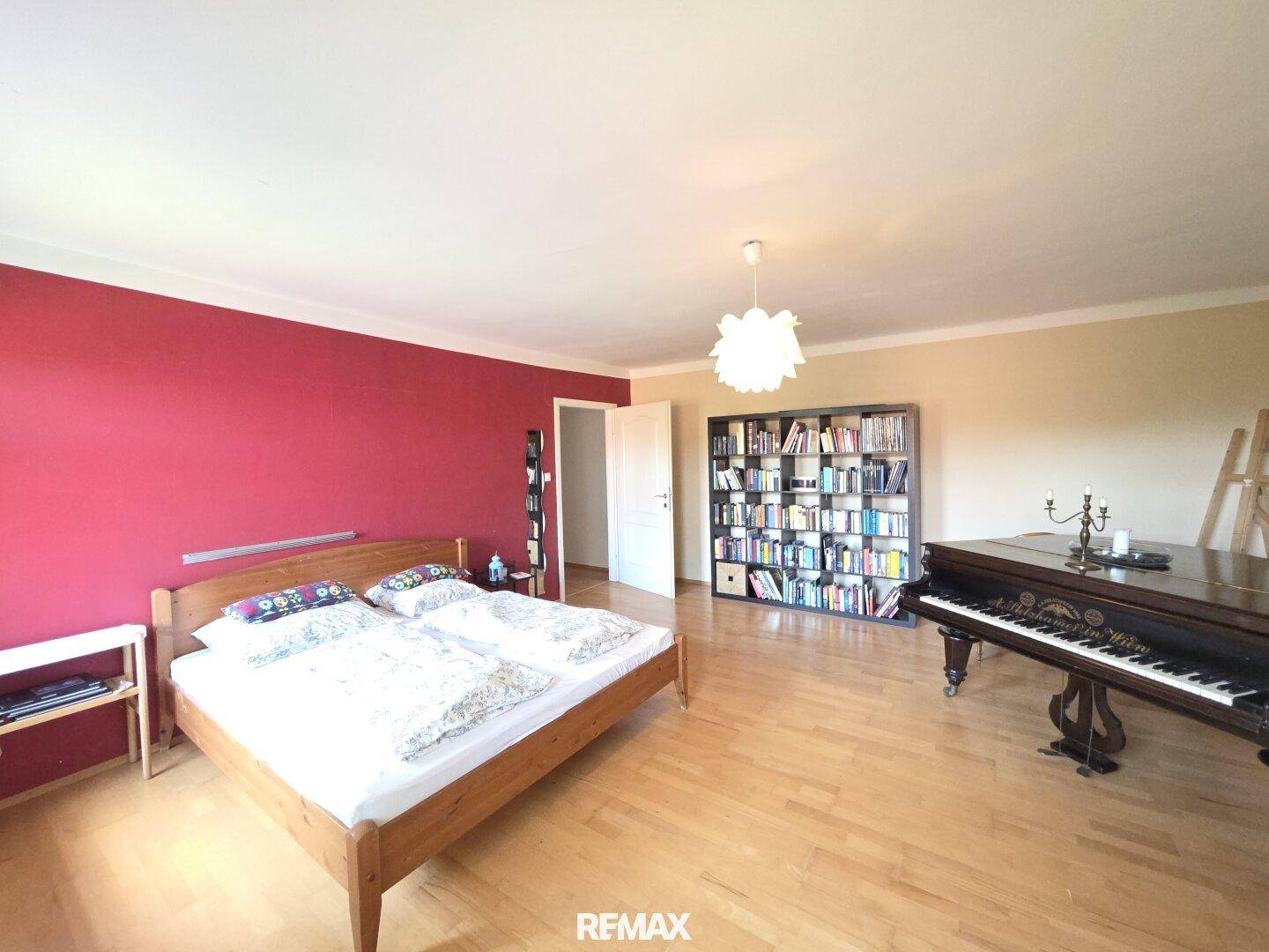 Geräumiges Schlafzimmer mit Holzboden, Doppelbett, Bücherregal und einem Flügel.