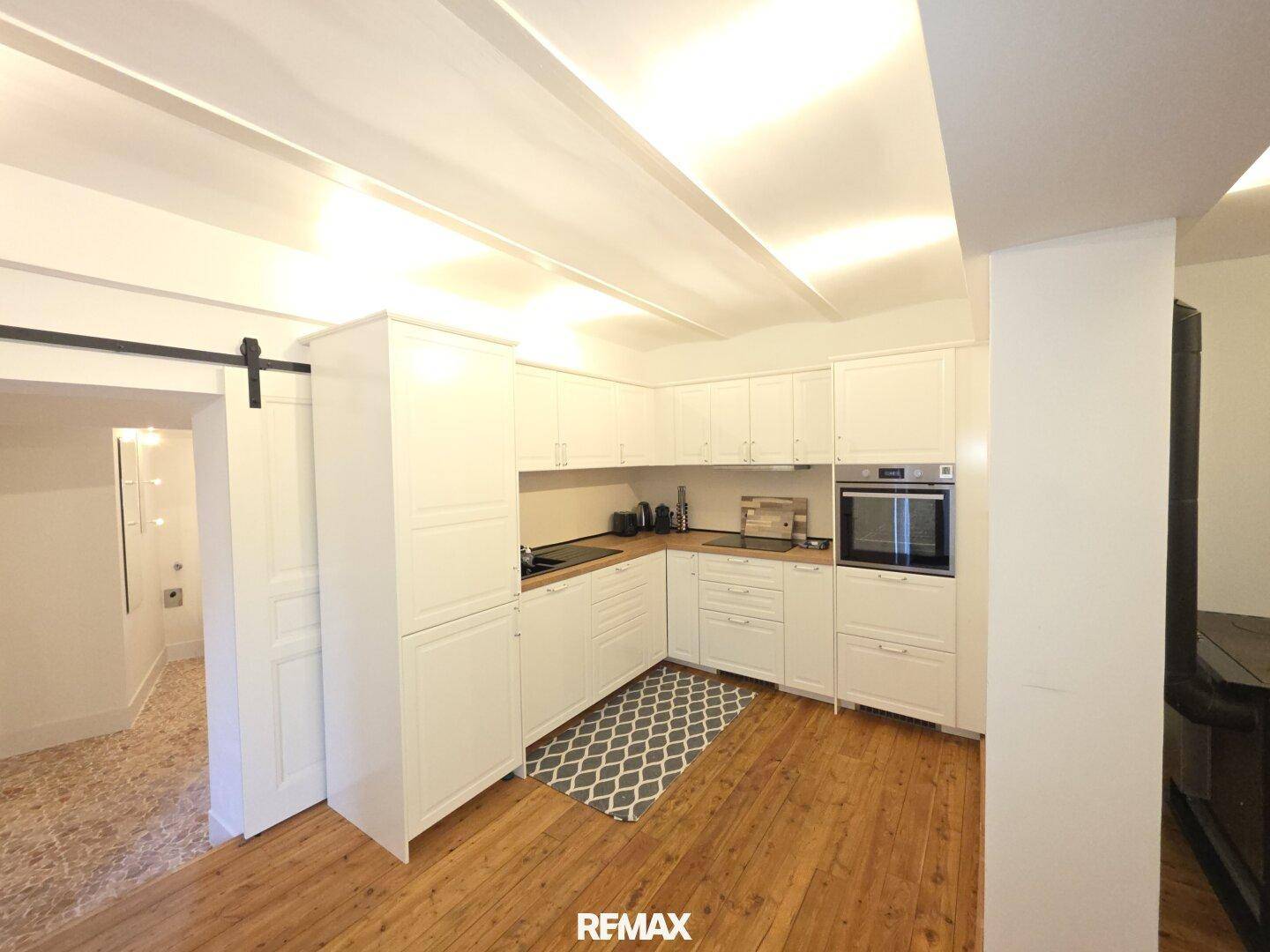 Moderne weiße Küche mit Holzboden, integrierten Geräten und Schiebetür.