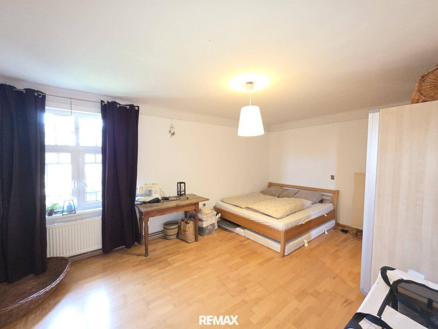 Schlafzimmer mit Holzboden, Doppelbett, Schreibtisch und großen Fenstern.
