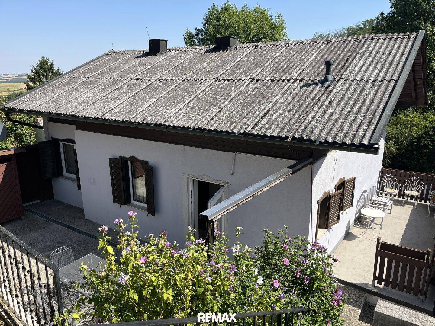 Rückseite des Hauses mit einer möblierten Terrasse und Blick auf die umliegende Landschaft.
