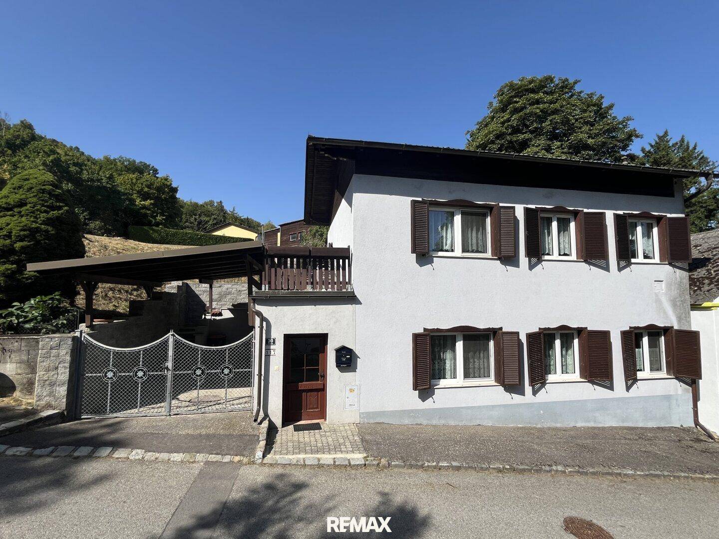 Ansicht des Einfamilienhauses mit traditionellen Fensterläden, Carport und Zugang zum Grundstück.