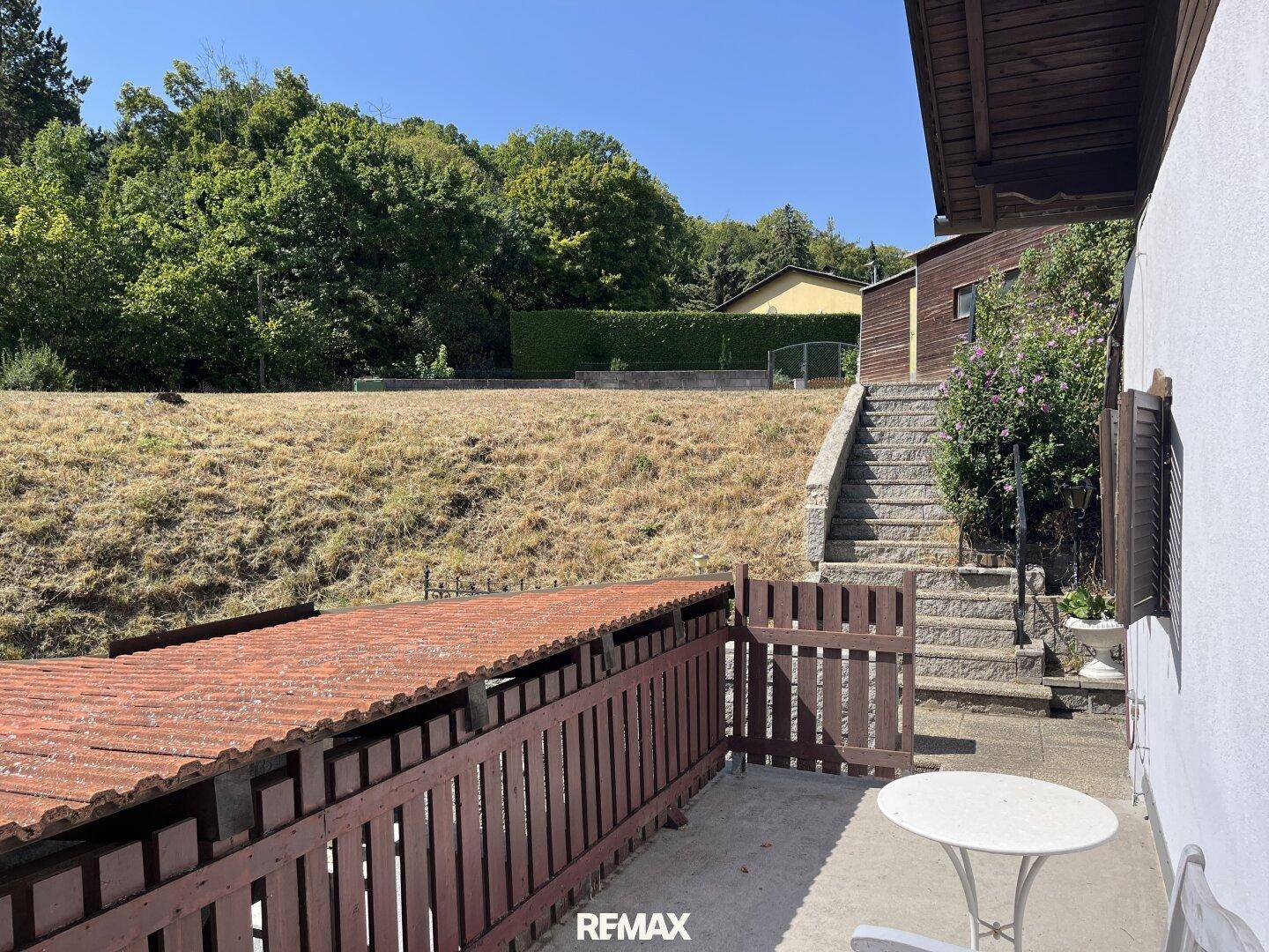 Großer, leicht abfallender Gartenbereich mit Steintreppe und Blick auf die bewaldete Umgebung.