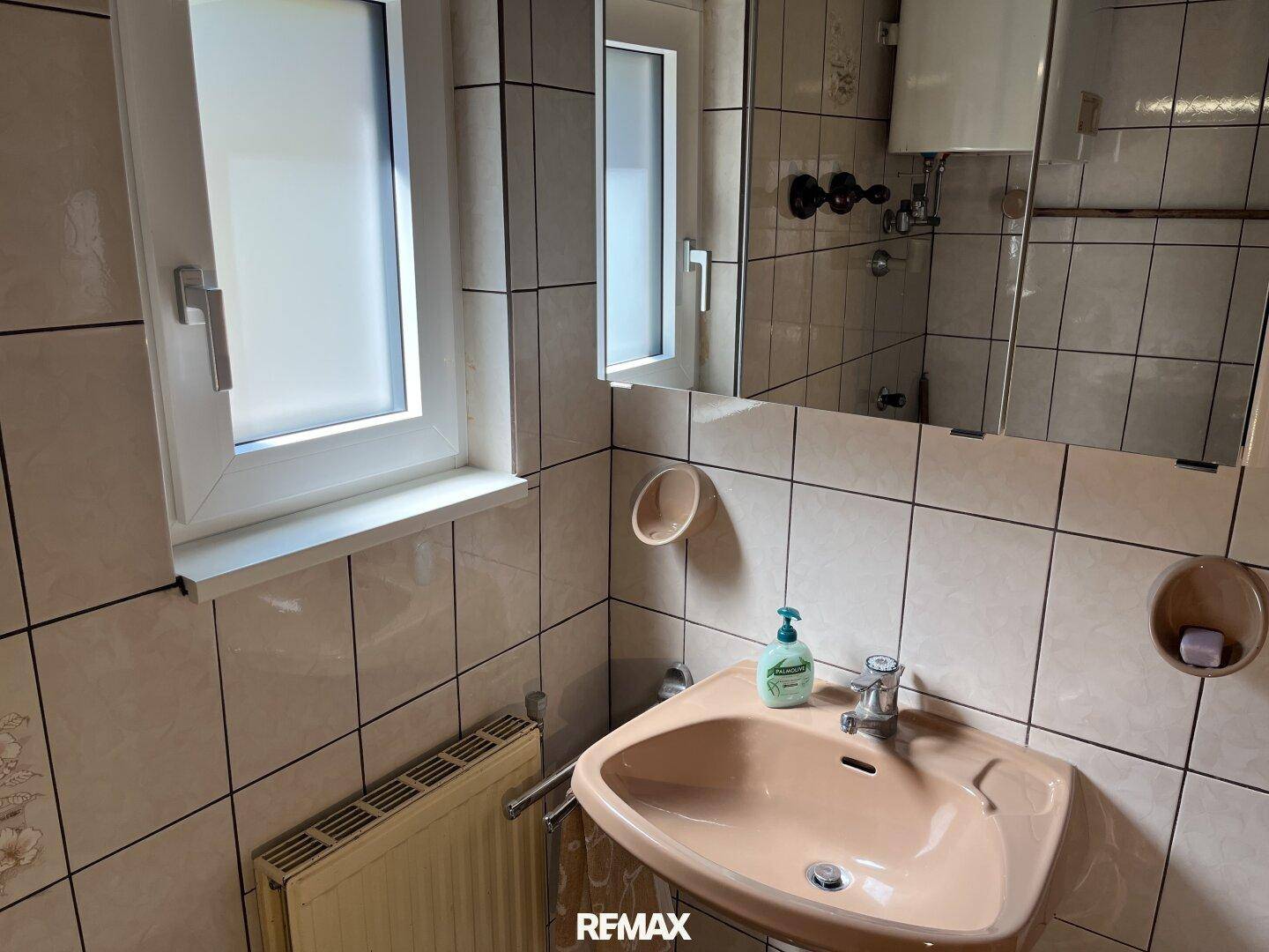 Badezimmer mit Waschbecken, Spiegelschrank und Fenster für Tageslicht.