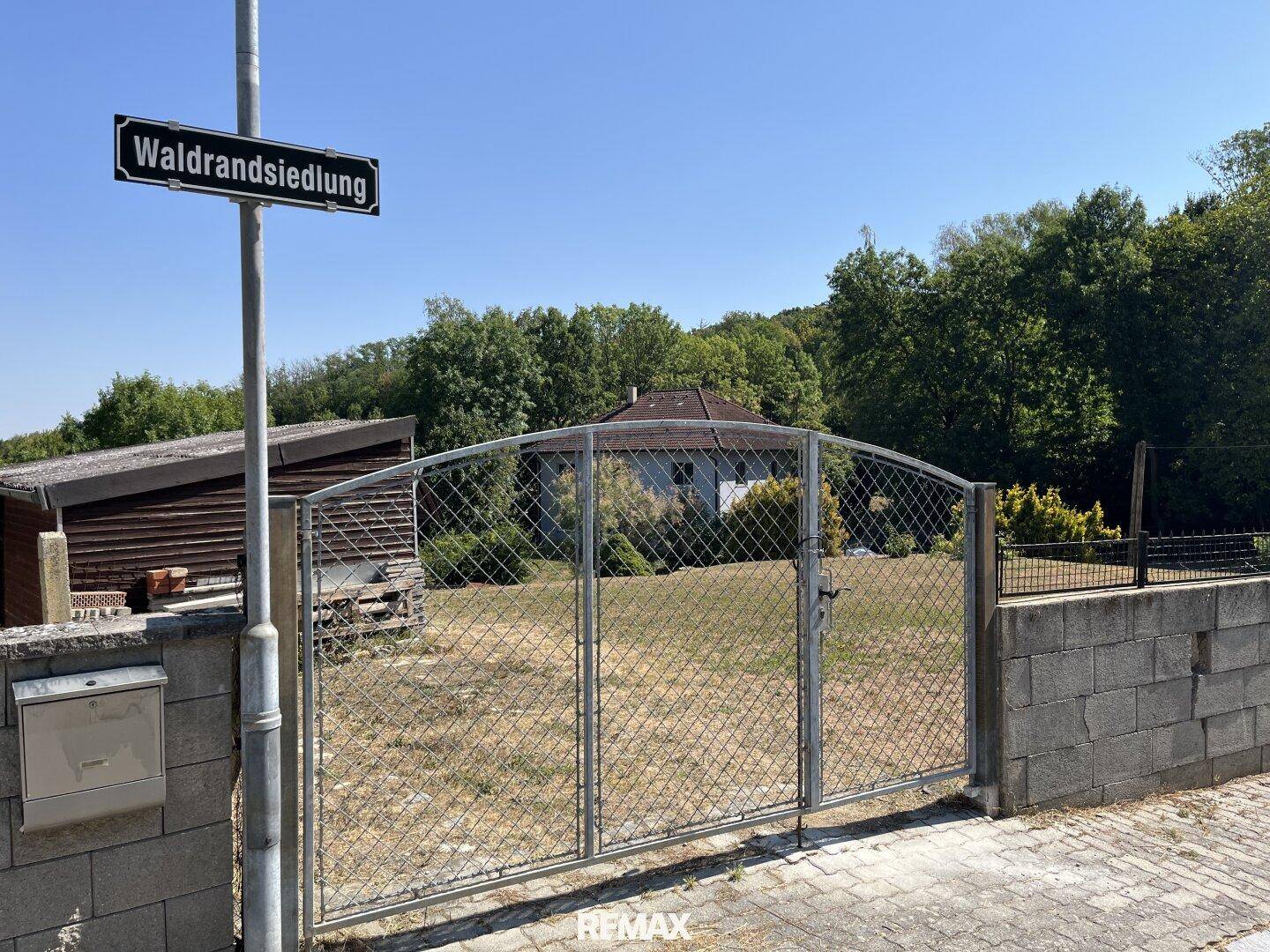 Eingangsbereich einer Immobilie mit Metalltor, Briefkasten und Straßenschild "Waldrandsiedlung".