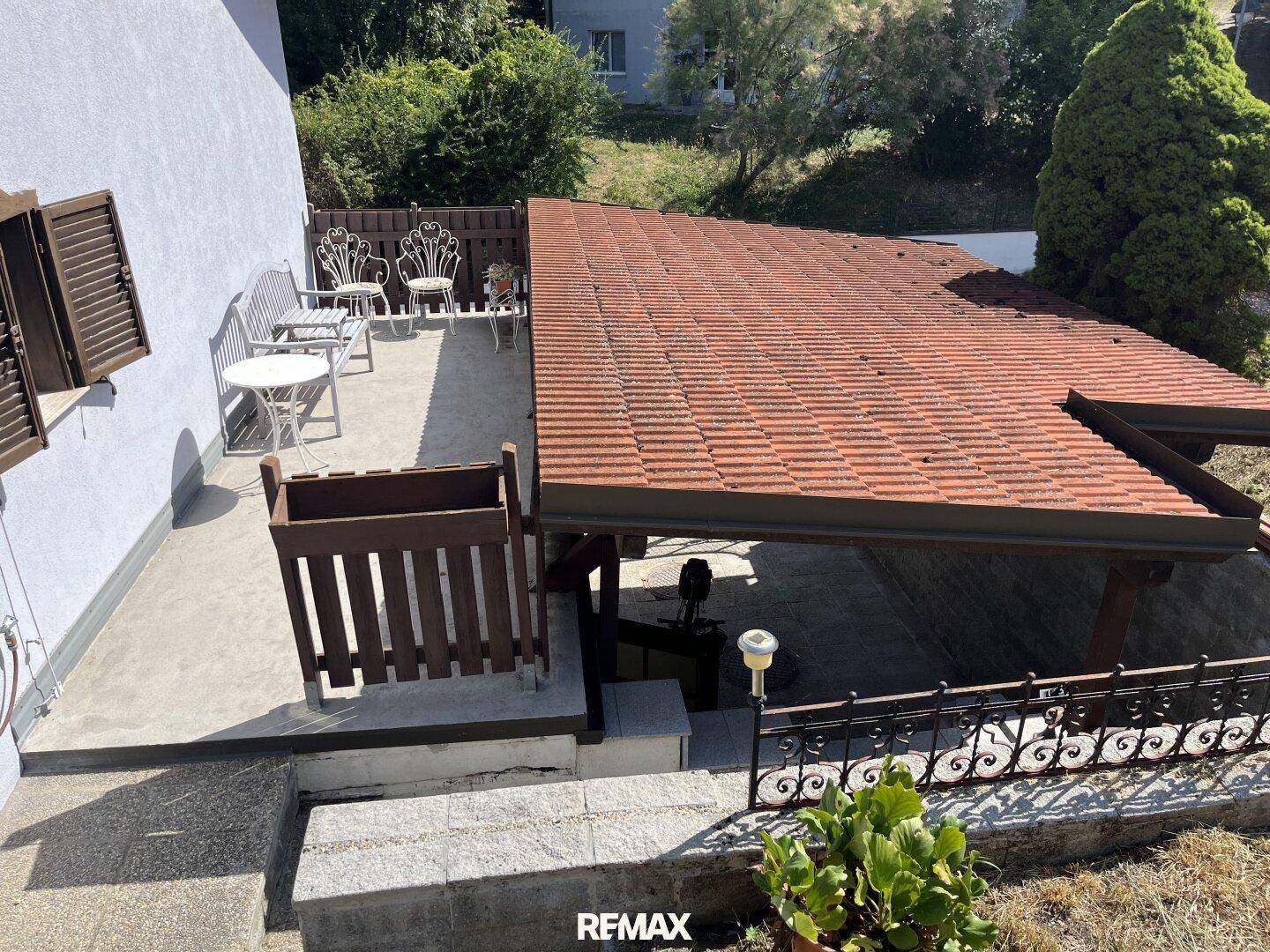 Überdachte Terrasse mit Gartenmöbeln und Blick auf die Umgebung, daneben ein Carport.
