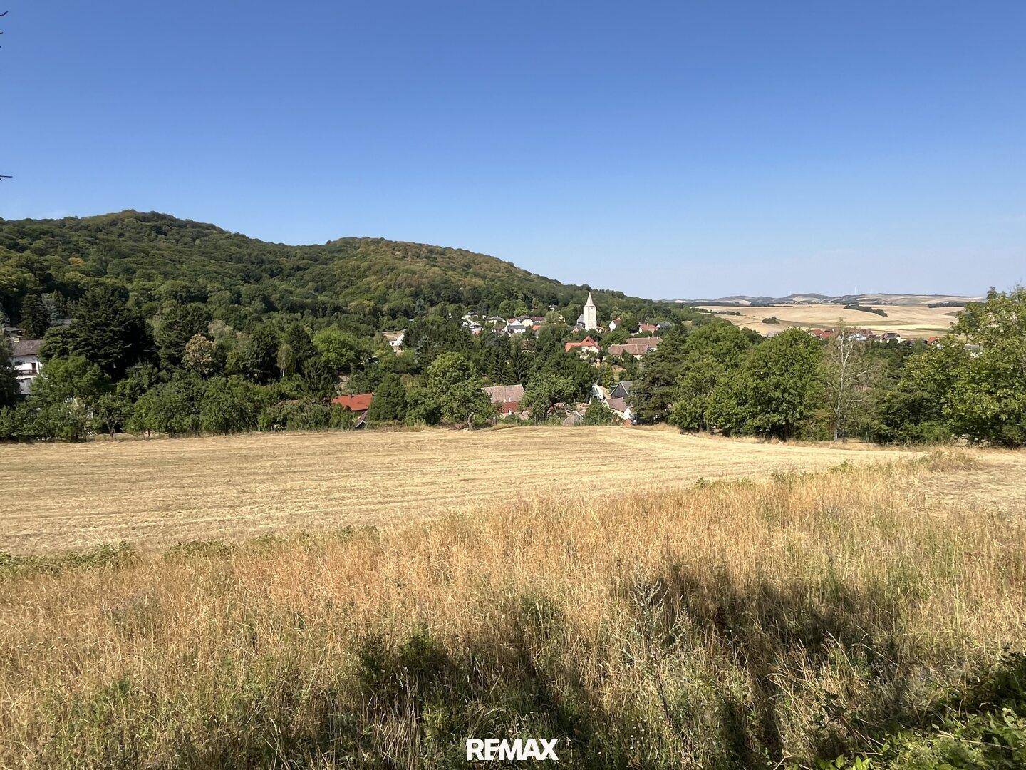 Panoramablick über weite Felder und eine malerische Dorflandschaft mit bewaldeten Hügeln.