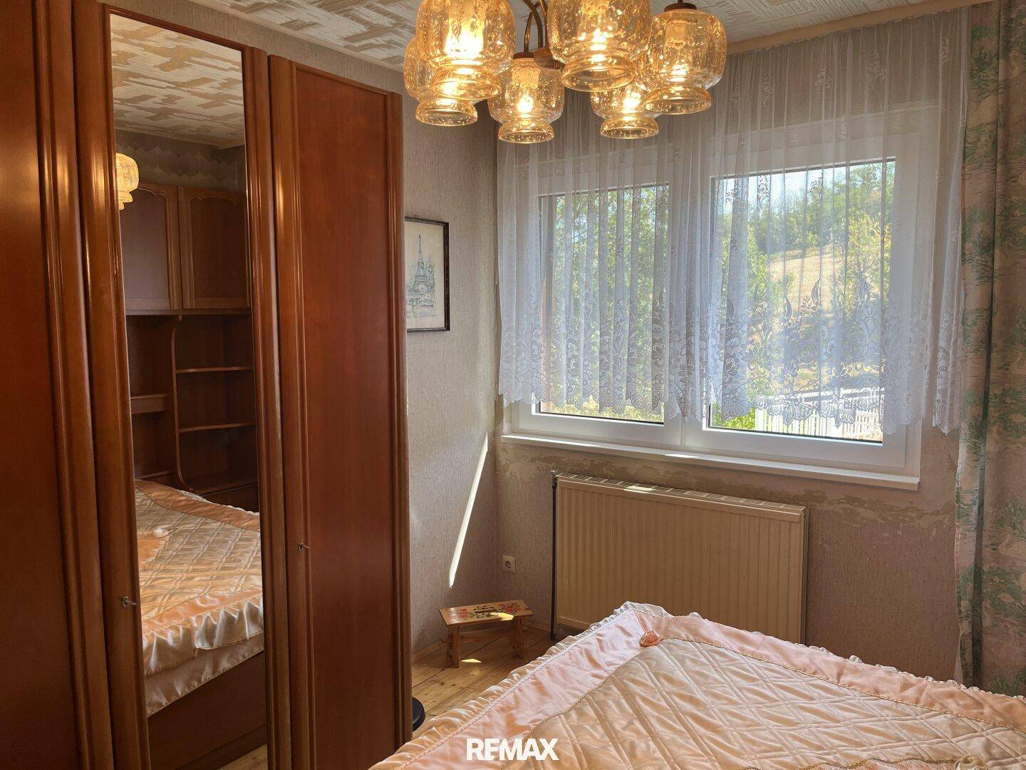 Helles Schlafzimmer mit Holzboden, Fenster und traditioneller Einrichtung.
