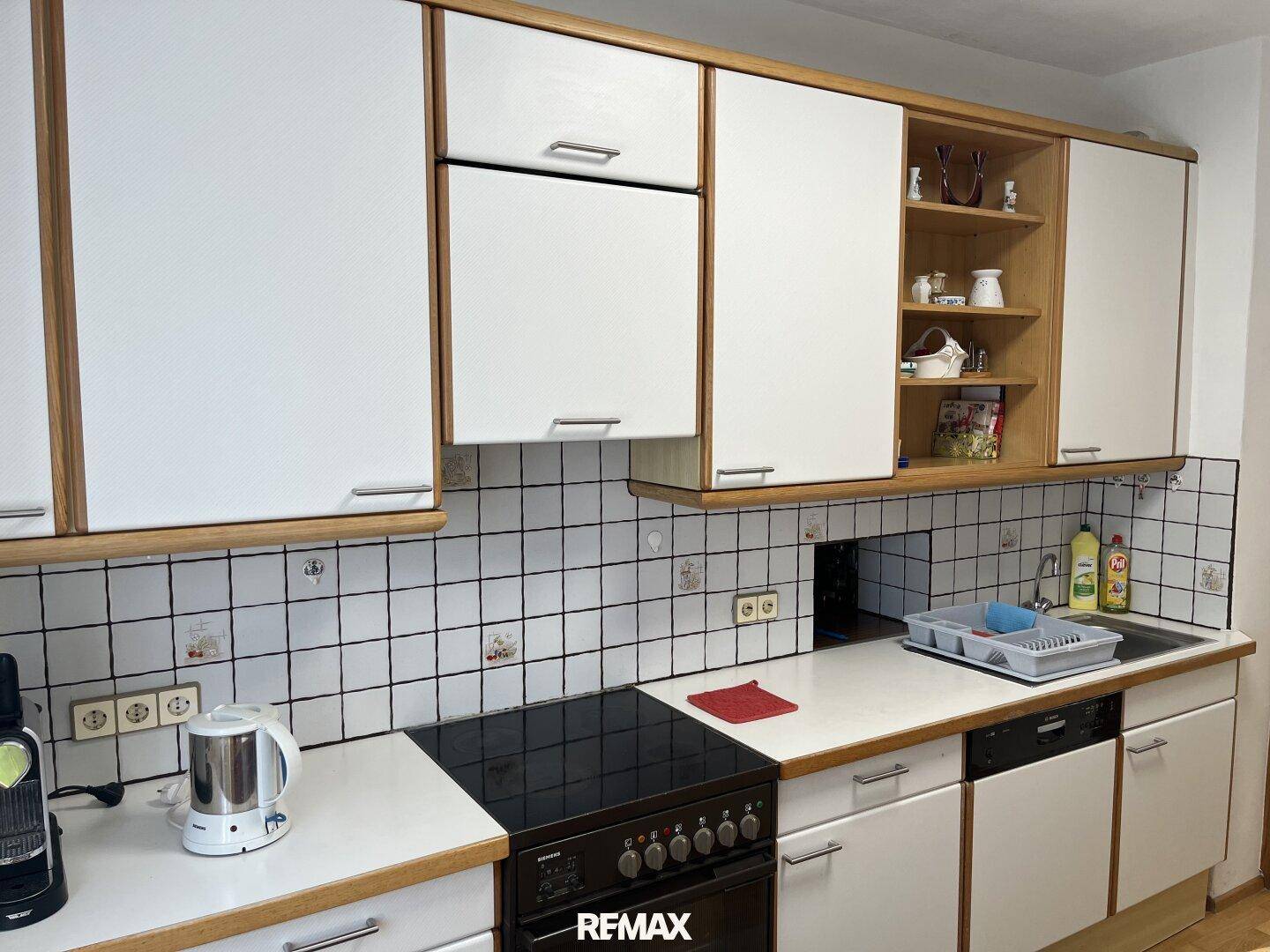 Funktionale Küche mit weißen Schränken, Holzrahmen und gefliestem Fliesenspiegel.