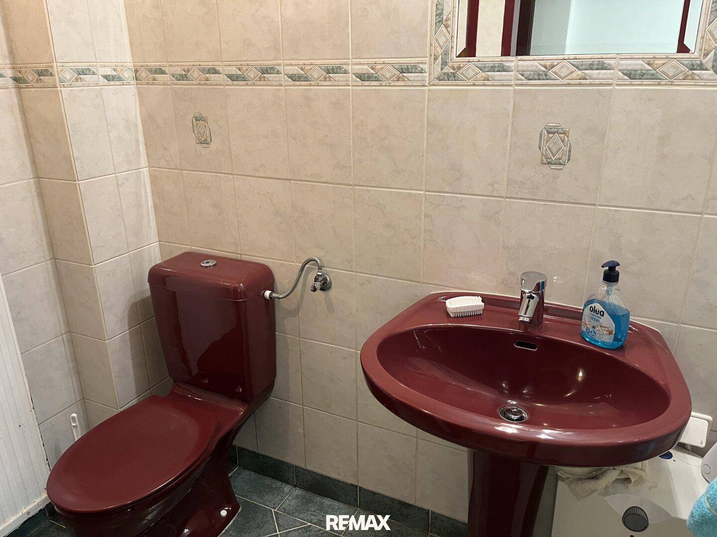 Gäste-WC mit roten Sanitärobjekten, Fliesen an Wänden und Boden.