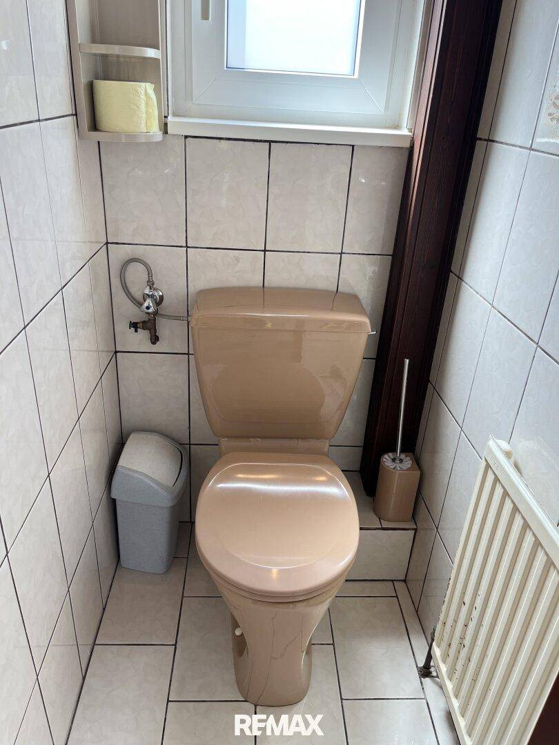 Separate Toilette mit beigefarbenem WC, Fliesen und Heizkörper.