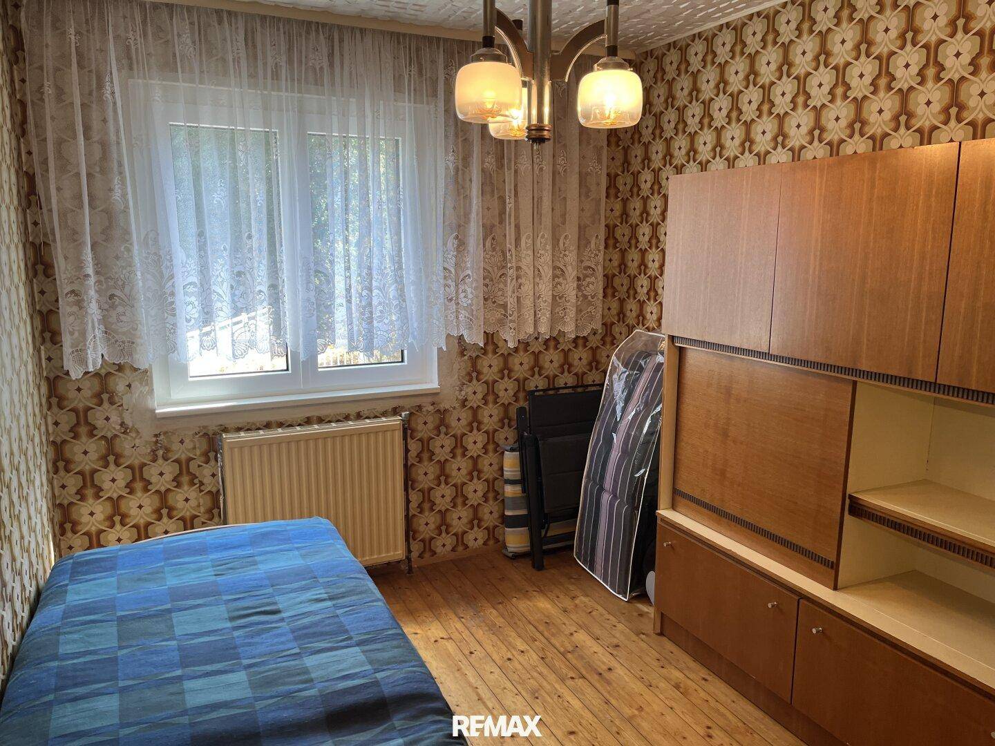 Kinderzimmer oder Gästezimmer mit Einzelbett, Holzboden und gemusterter Tapete.