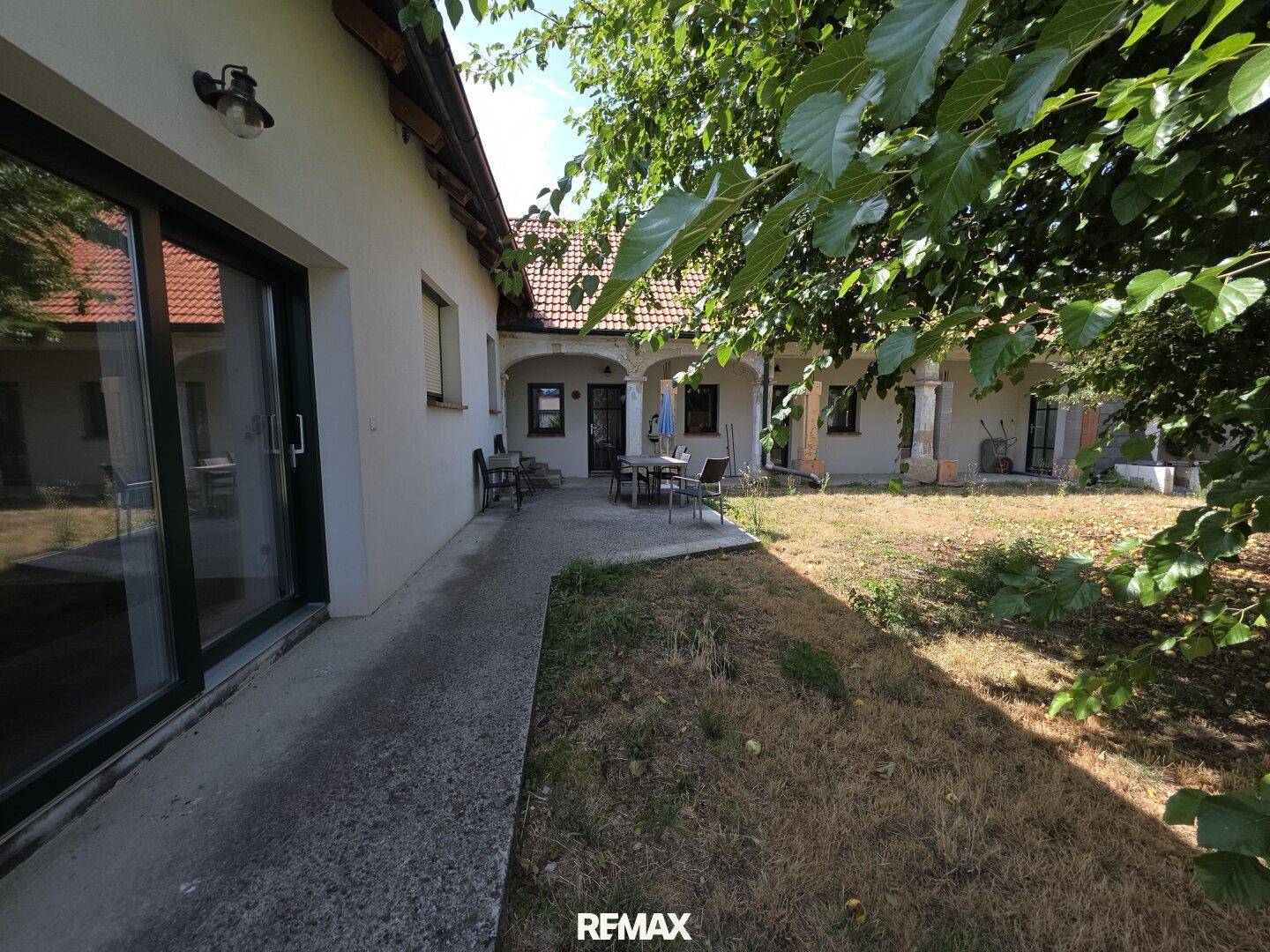 Blick vom Garten auf die Hausfassade mit einer großzügigen Terrasse und viel Grün.